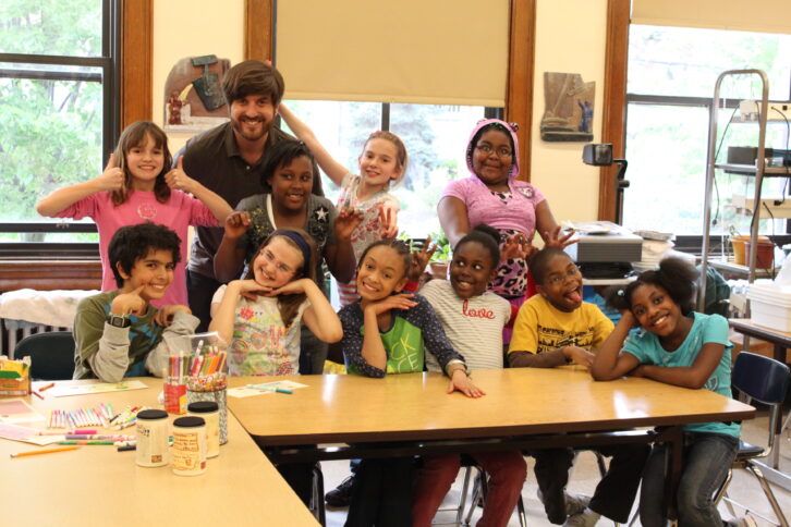 Ten youth and an adult smiling at the camera in a classroom