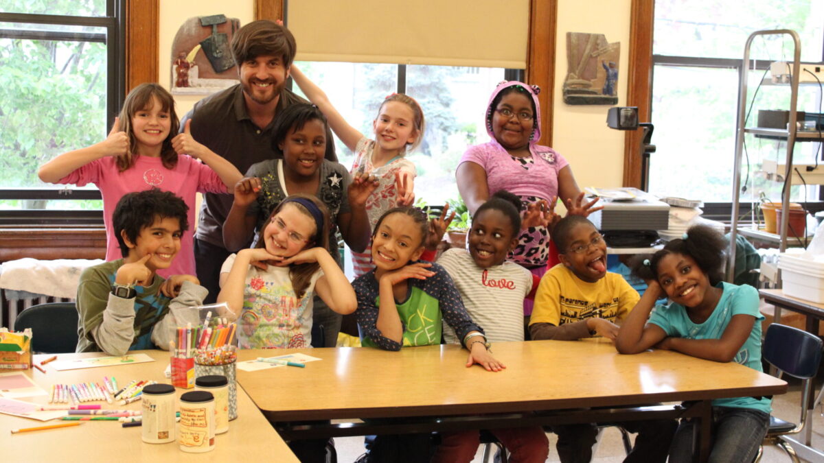 Ten youth and an adult smiling at the camera in a classroom