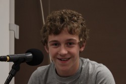 A teen smiling sitting behind a microphone