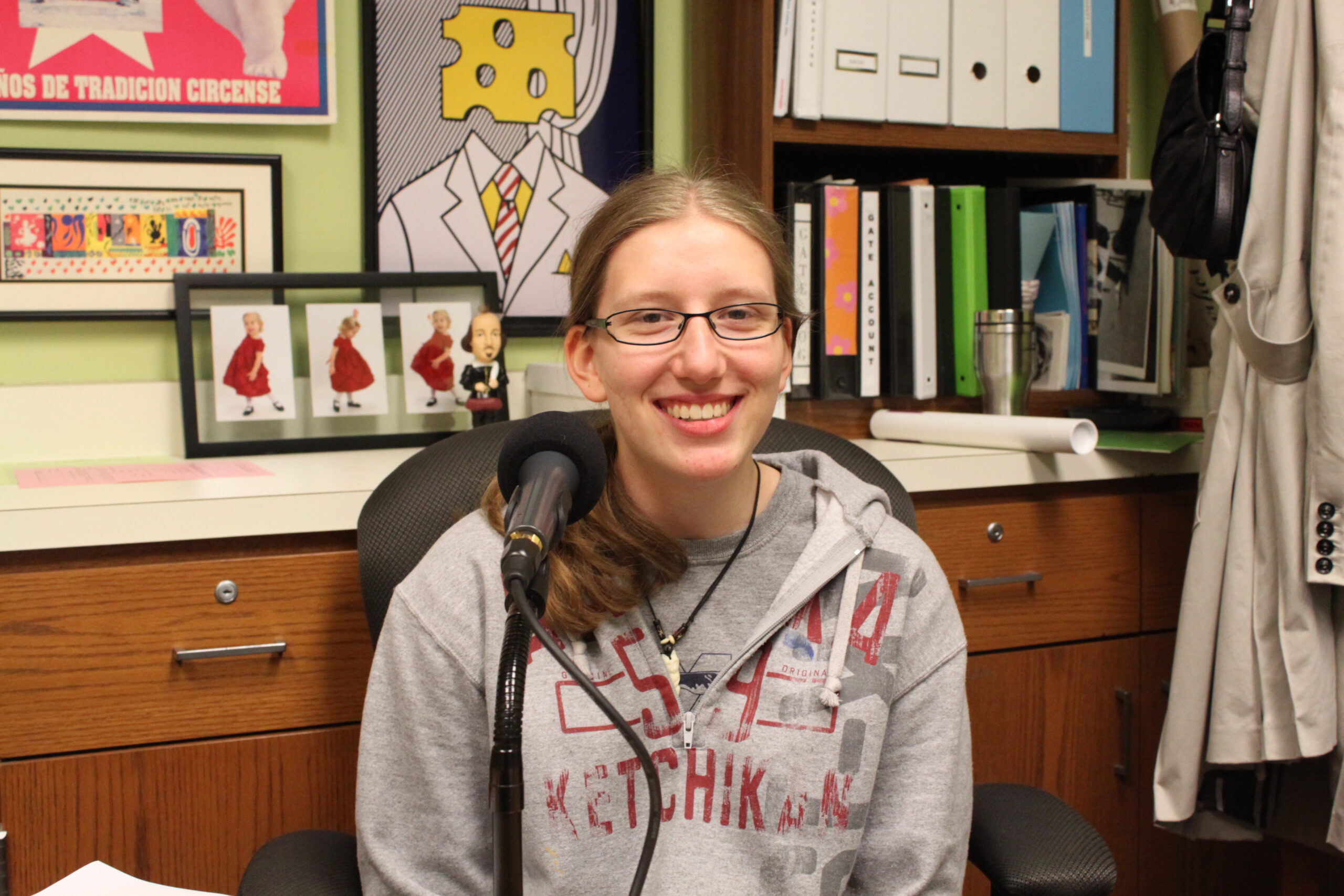 A teen smiling while sitting behind a microphone in a classroom