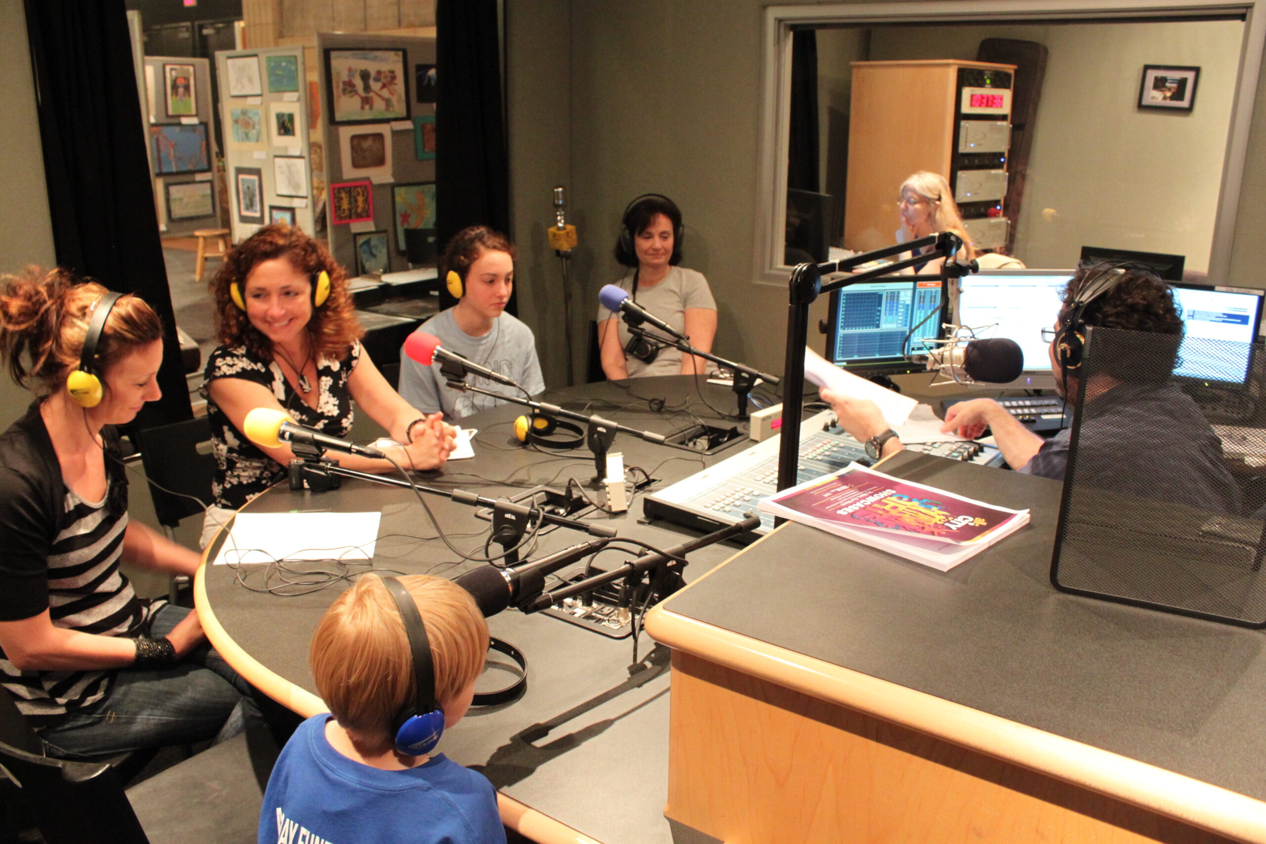 Three youth and two adults wearing headphones sitting behind microphones in a radio studio