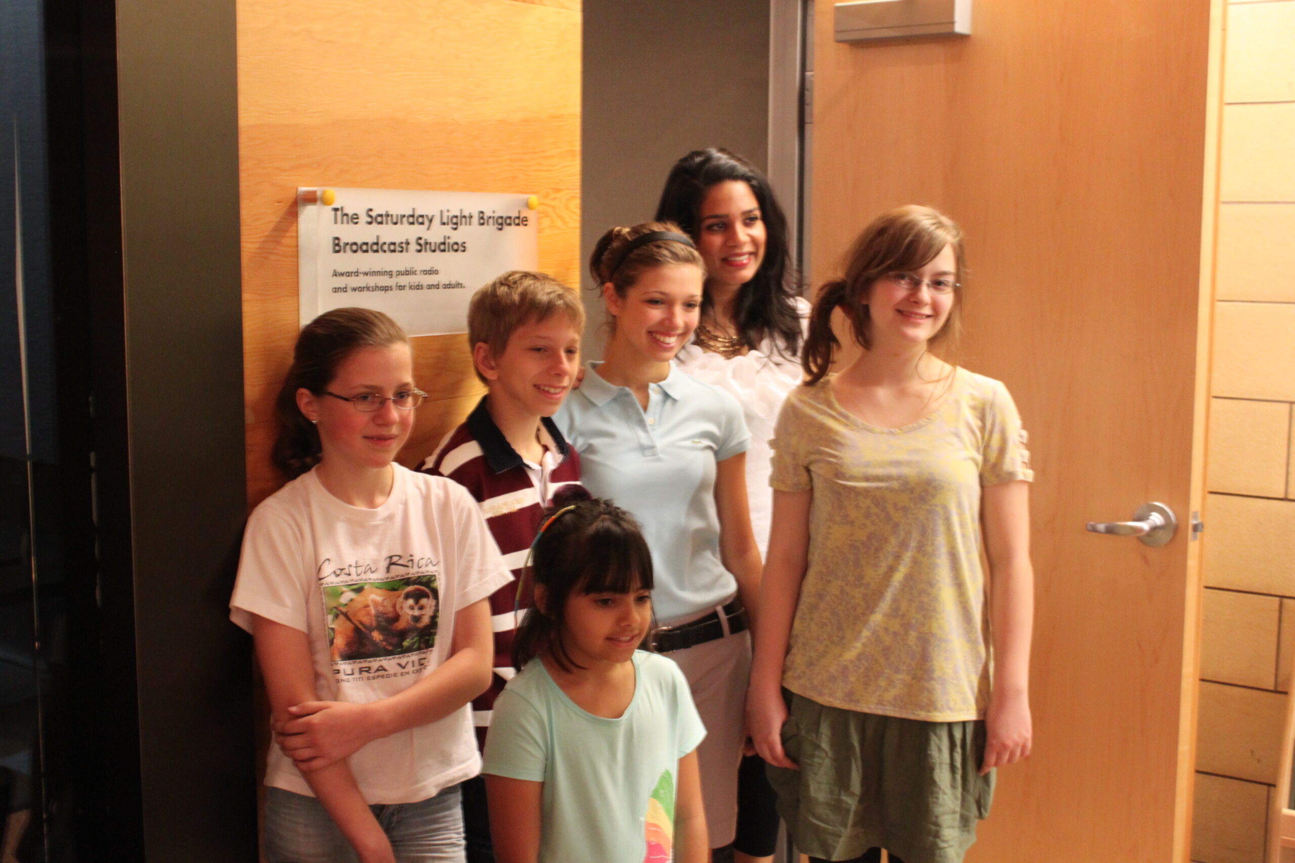 Five youth and an adult smiling and posing in front of a sign on a wooden wall