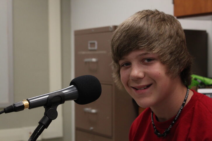 A youth smiling at the camera and standing behind a microphone