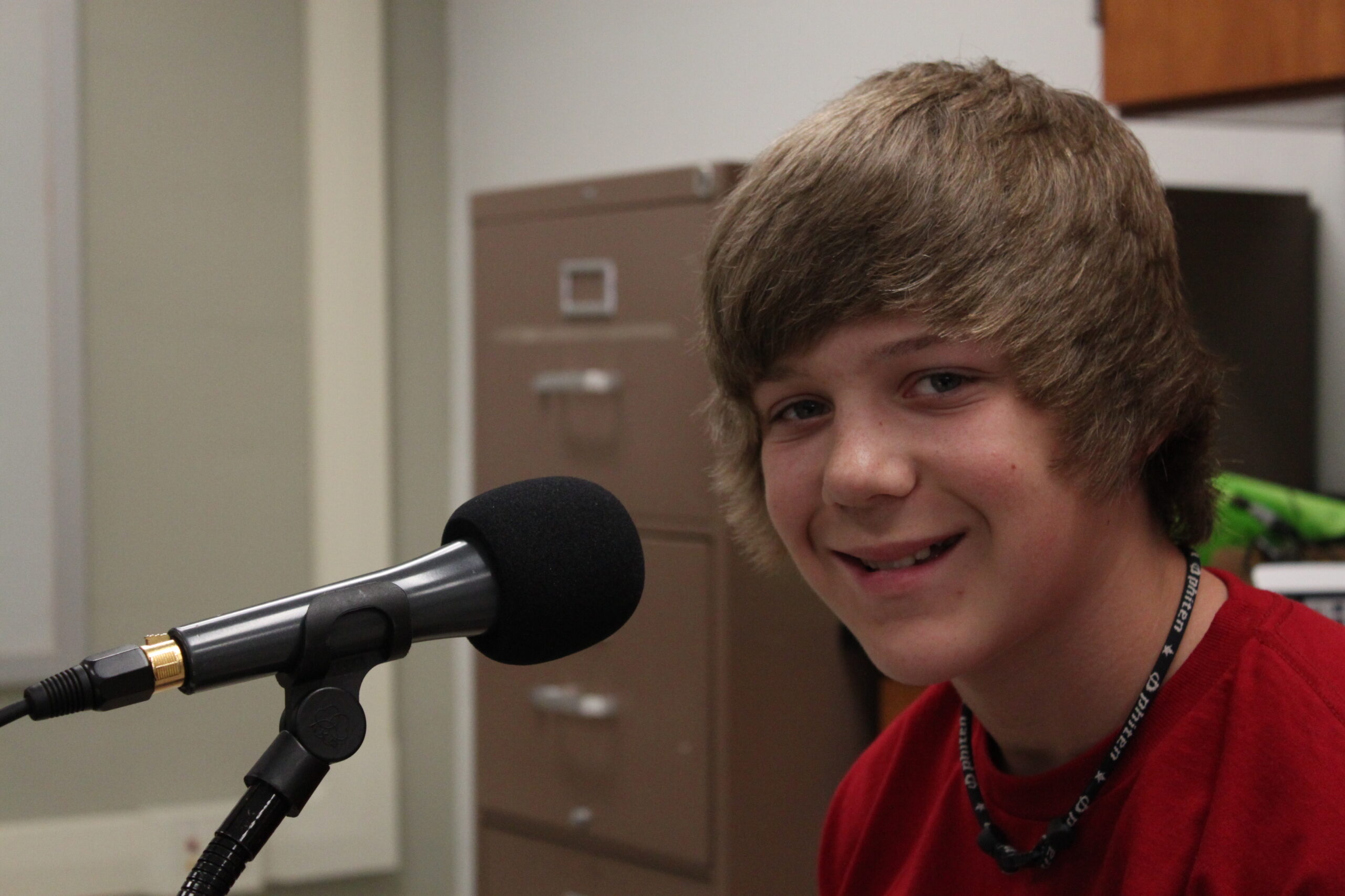 A youth smiling at the camera and standing behind a microphone