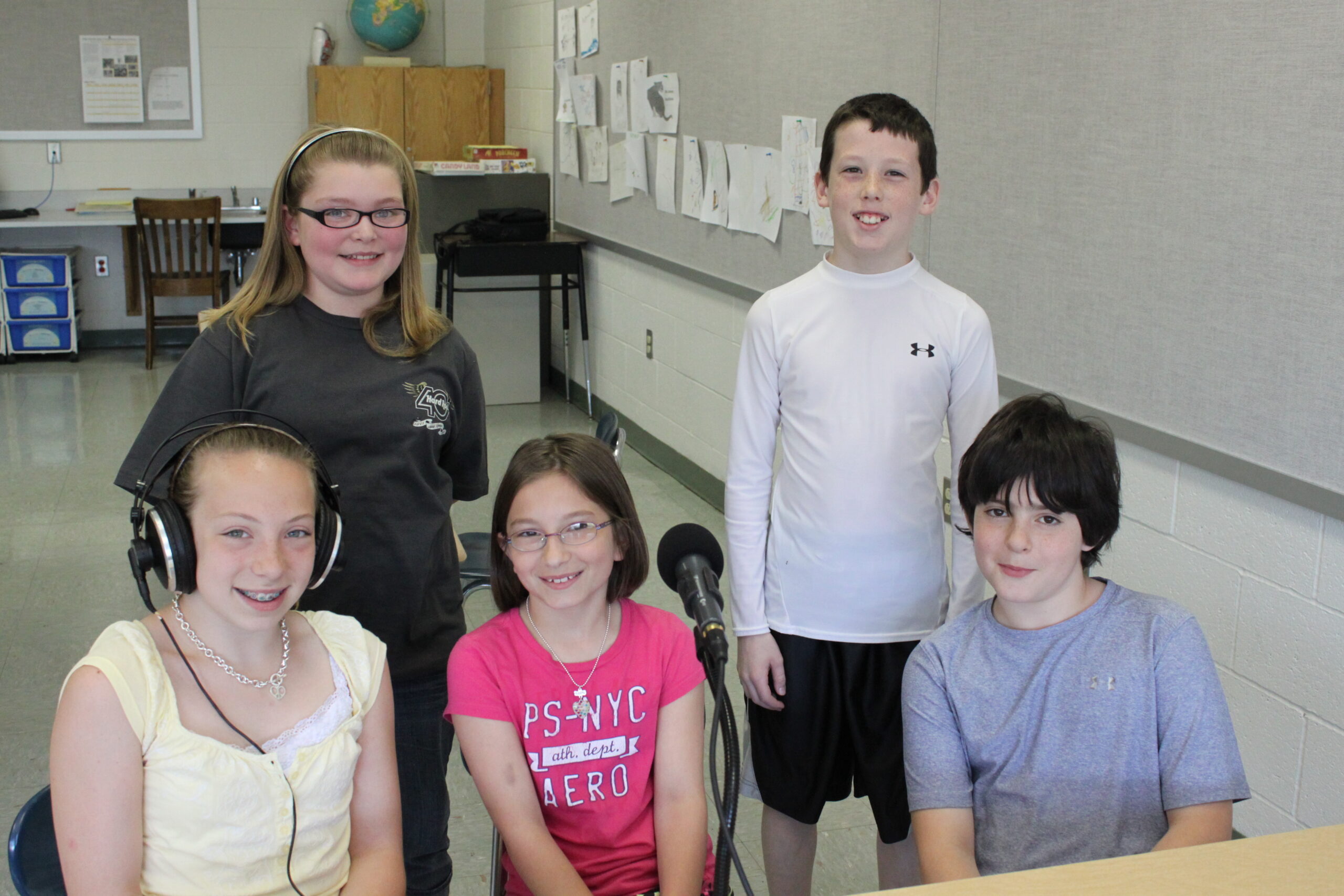 Five youth smiling behind a microphone in a classroom