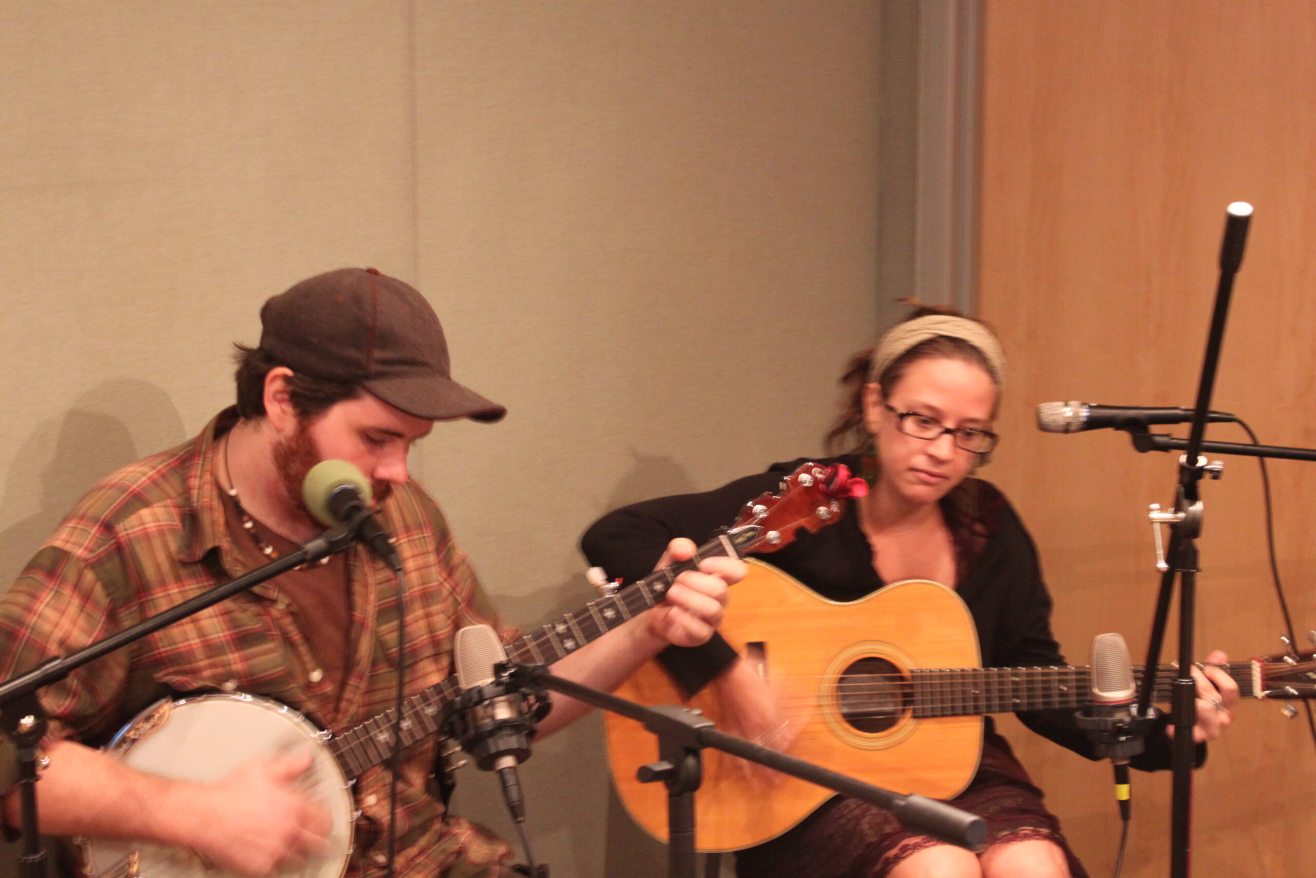 An adult playing banjo and an adult playing acoustic guitar in a radio studio