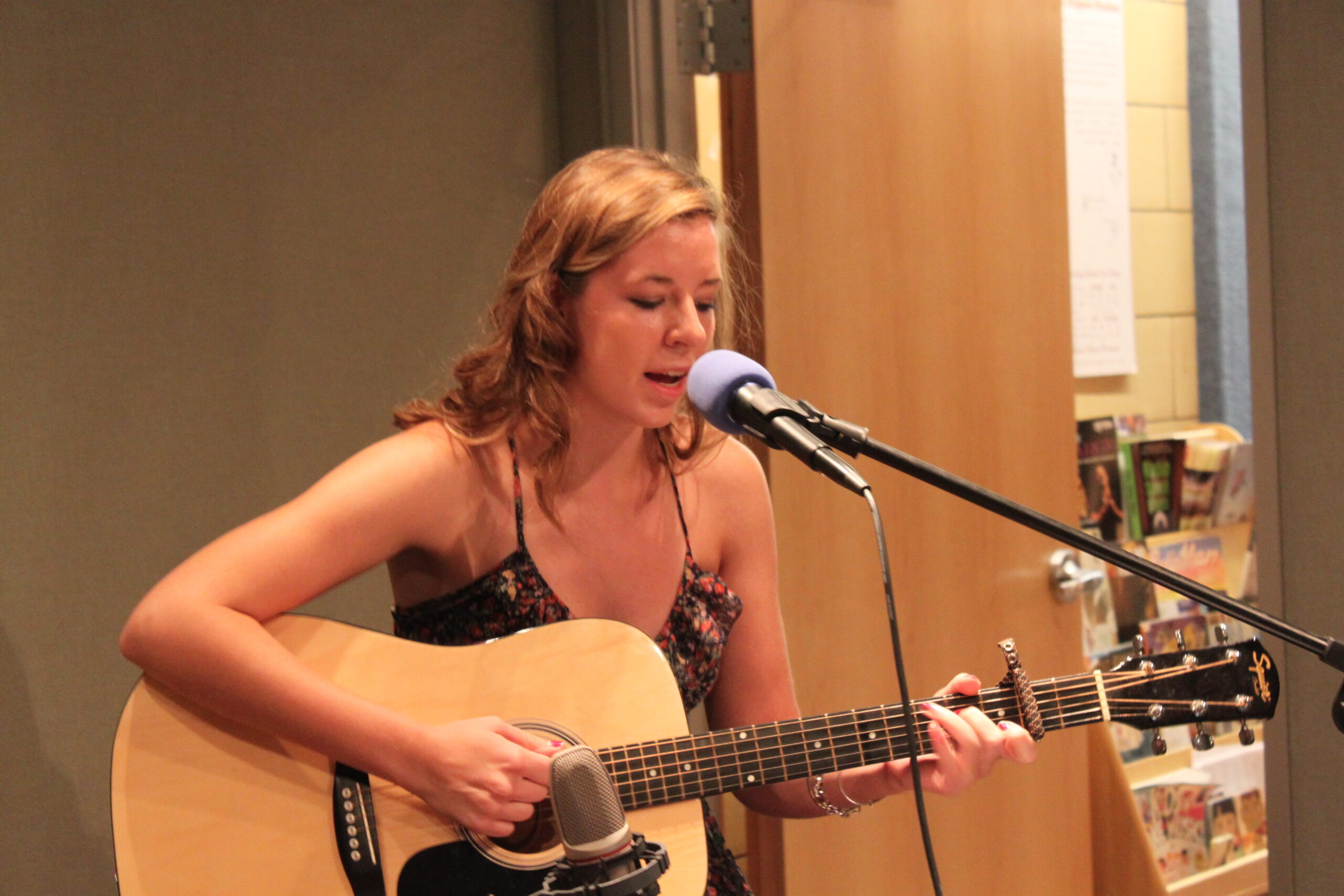 A teen playing an acoustic guitar and singing into a microphone in a radio studio