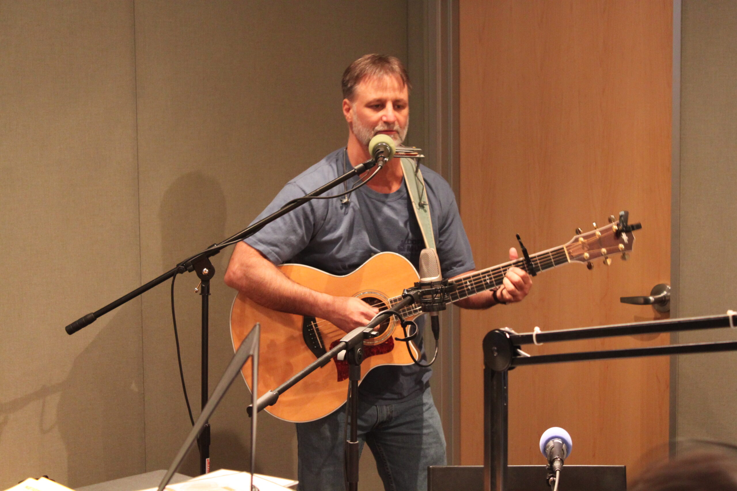 An adult playing an acoustic guitar and singing into a microphone in a radio studio
