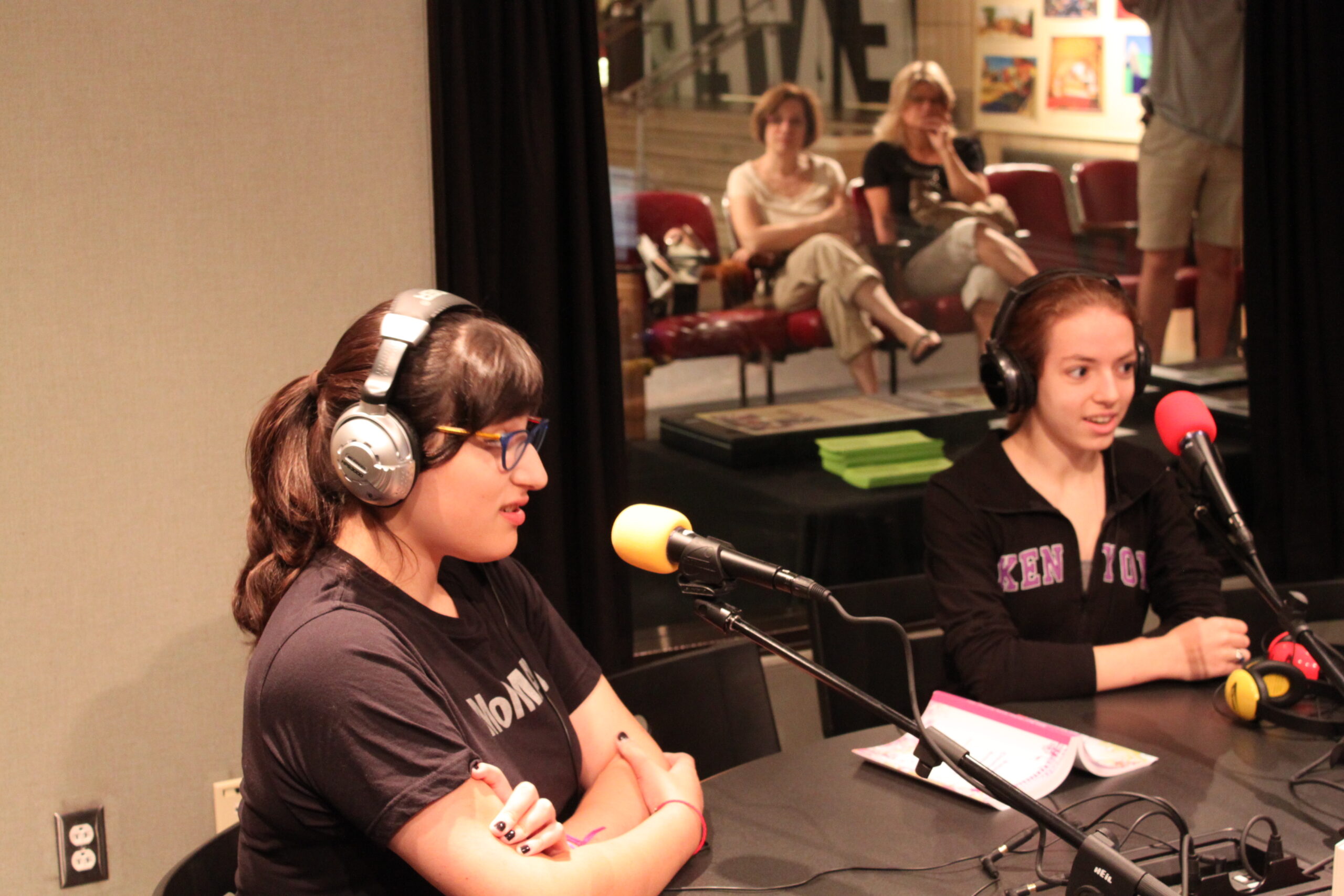 Two teens wearing headphones speaking into microphones in a radio studio