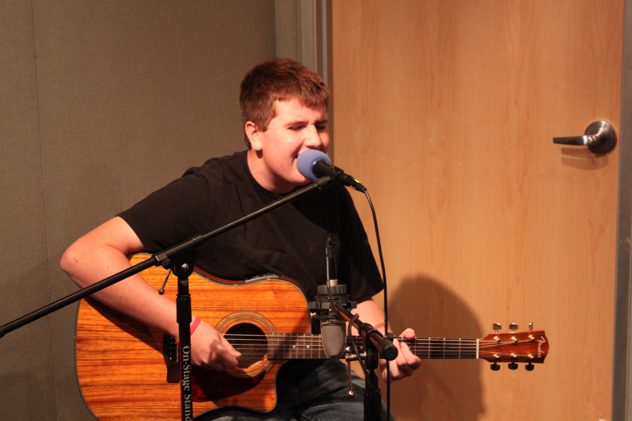 A teen playing acoustic guitar and singing into a microphone in a radio studio