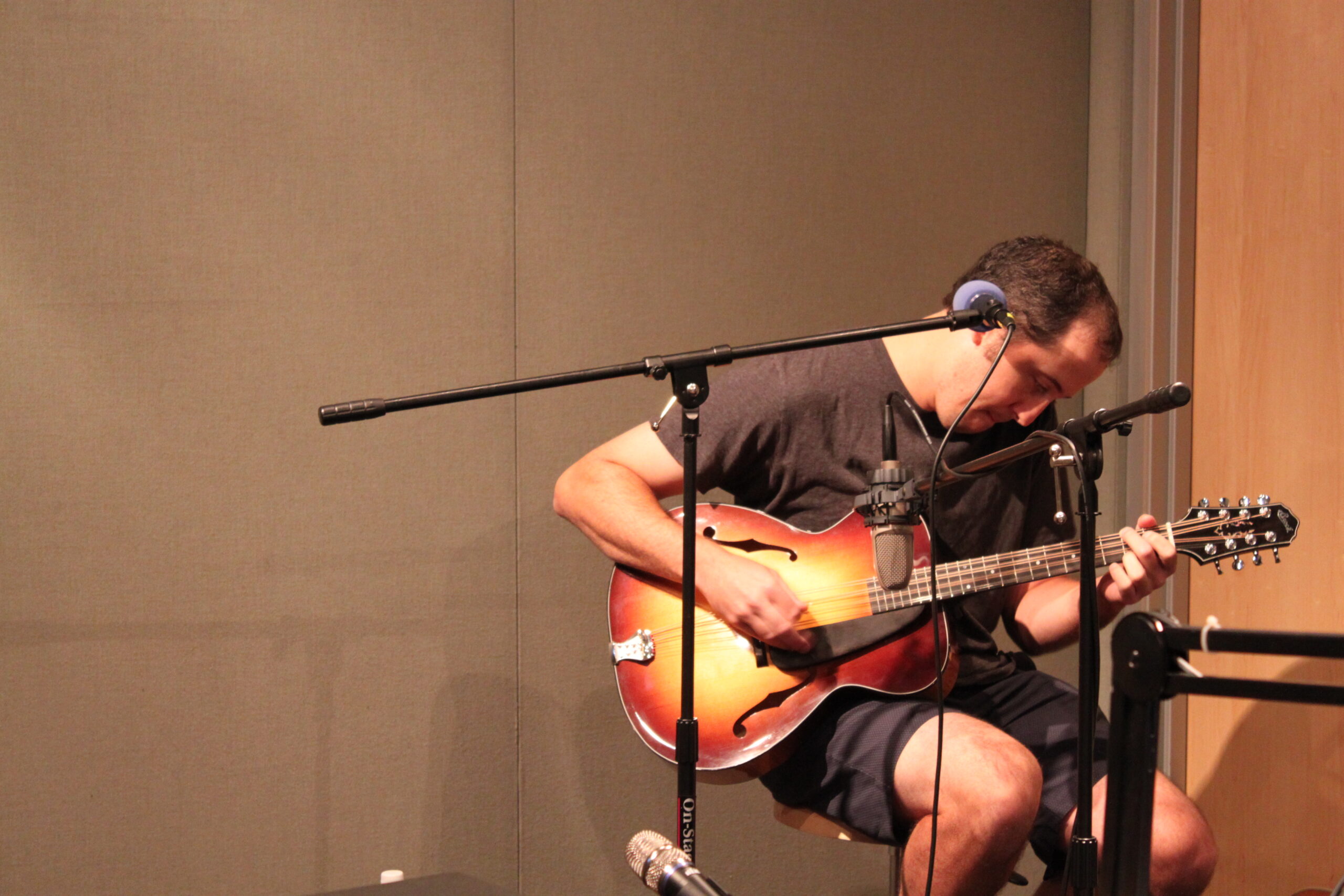 An adult playing an electric guitar and sitting behind microphones in a radio studio