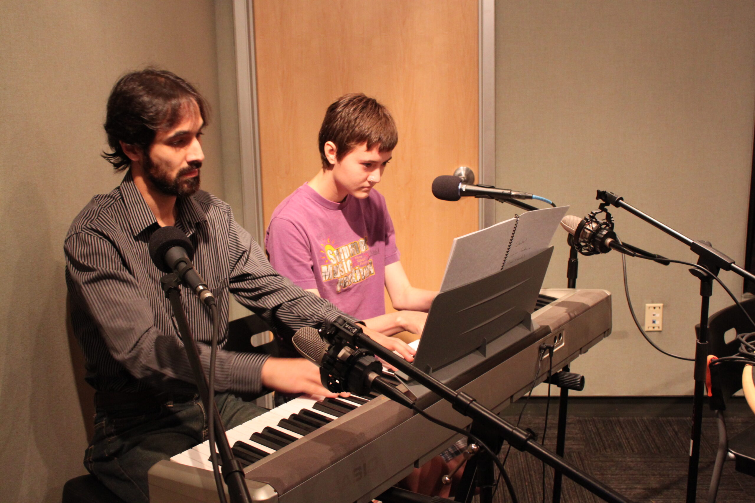 A youth and an adult playing a piano keyboard and looking at sheet music in a radio studio