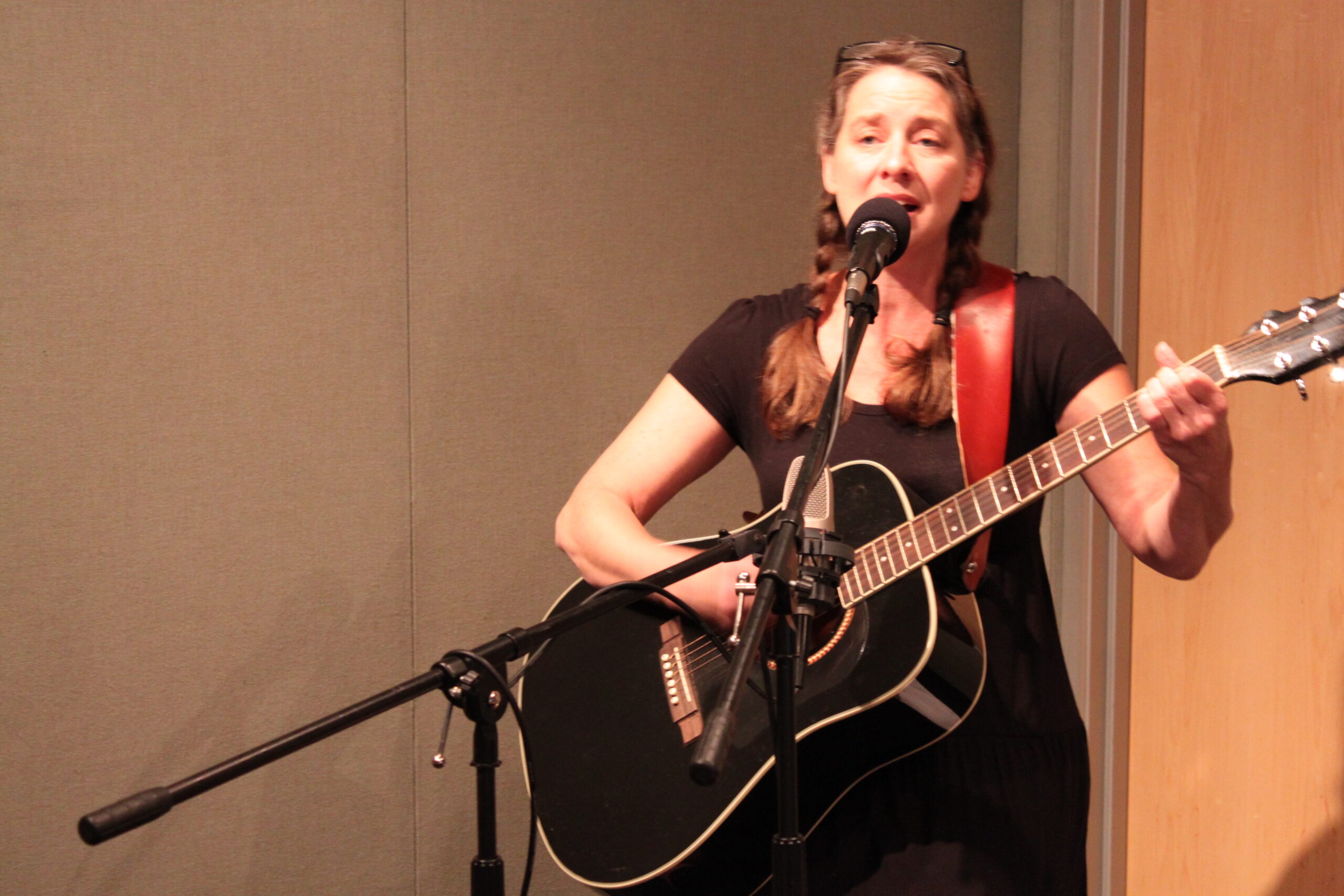 An adult playing an acoustic guitar and singing into a microphone in a radio studio