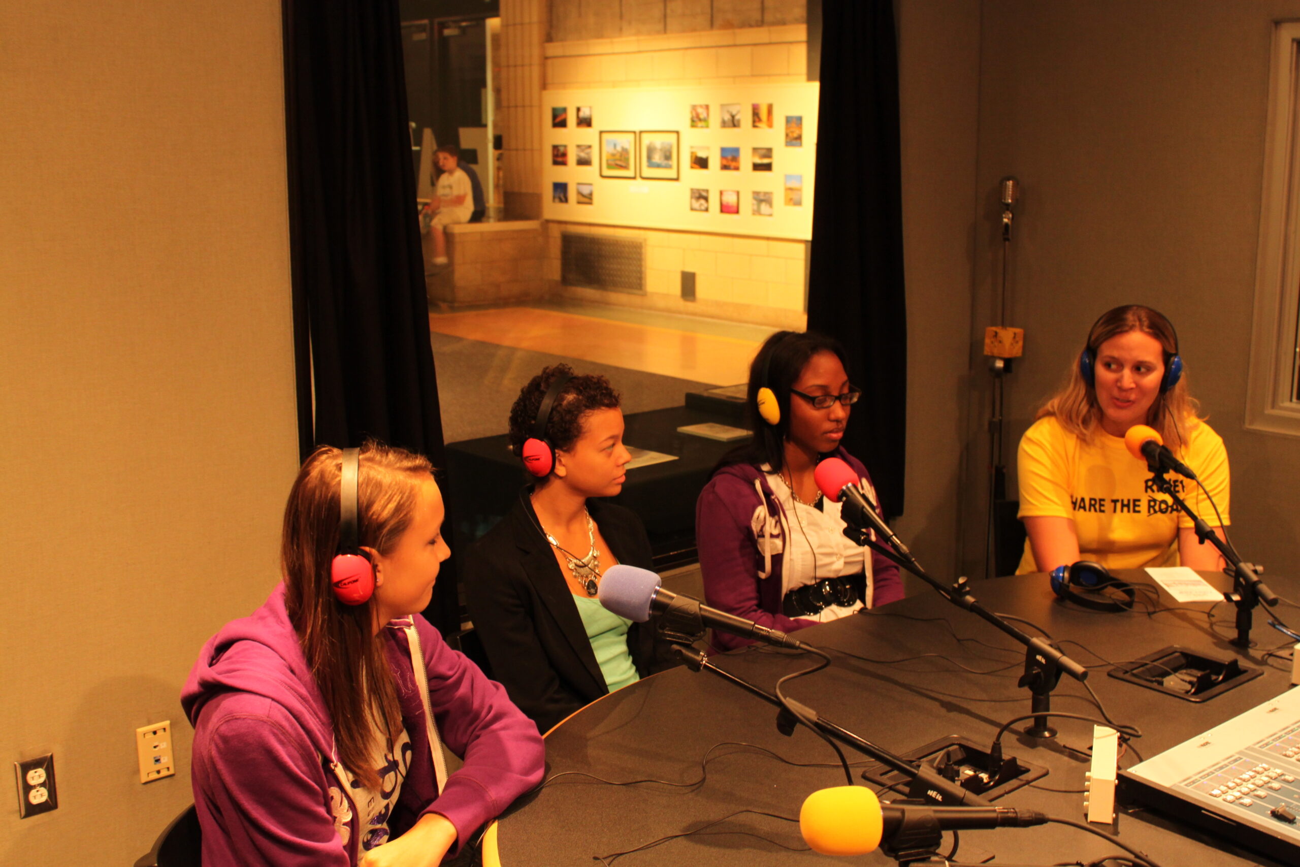 Three teens and an adult wearing headphones speaking into microphones in a radio studio
