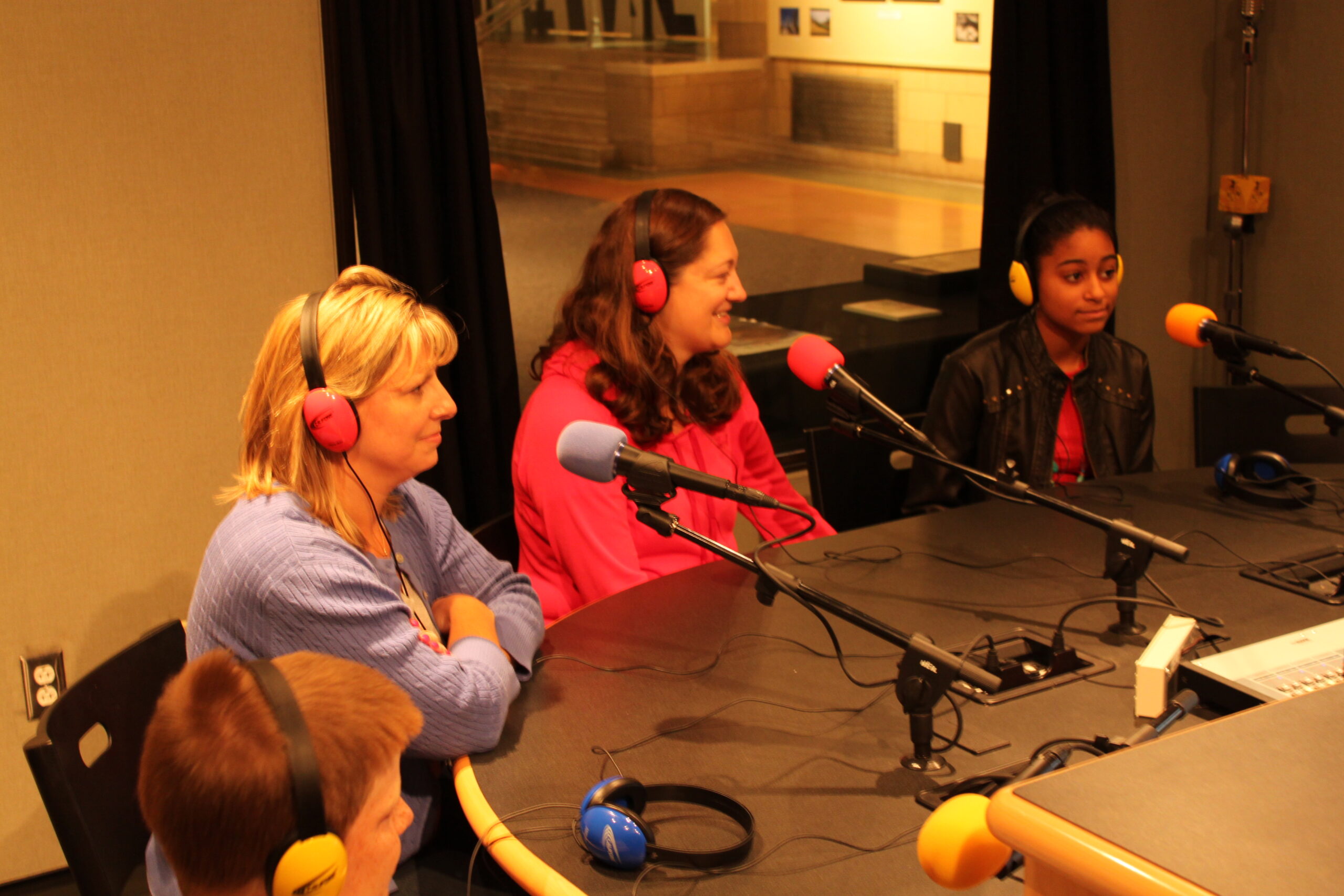 Two youth and two adults wearing headphones sitting behind microphones in a radio studio