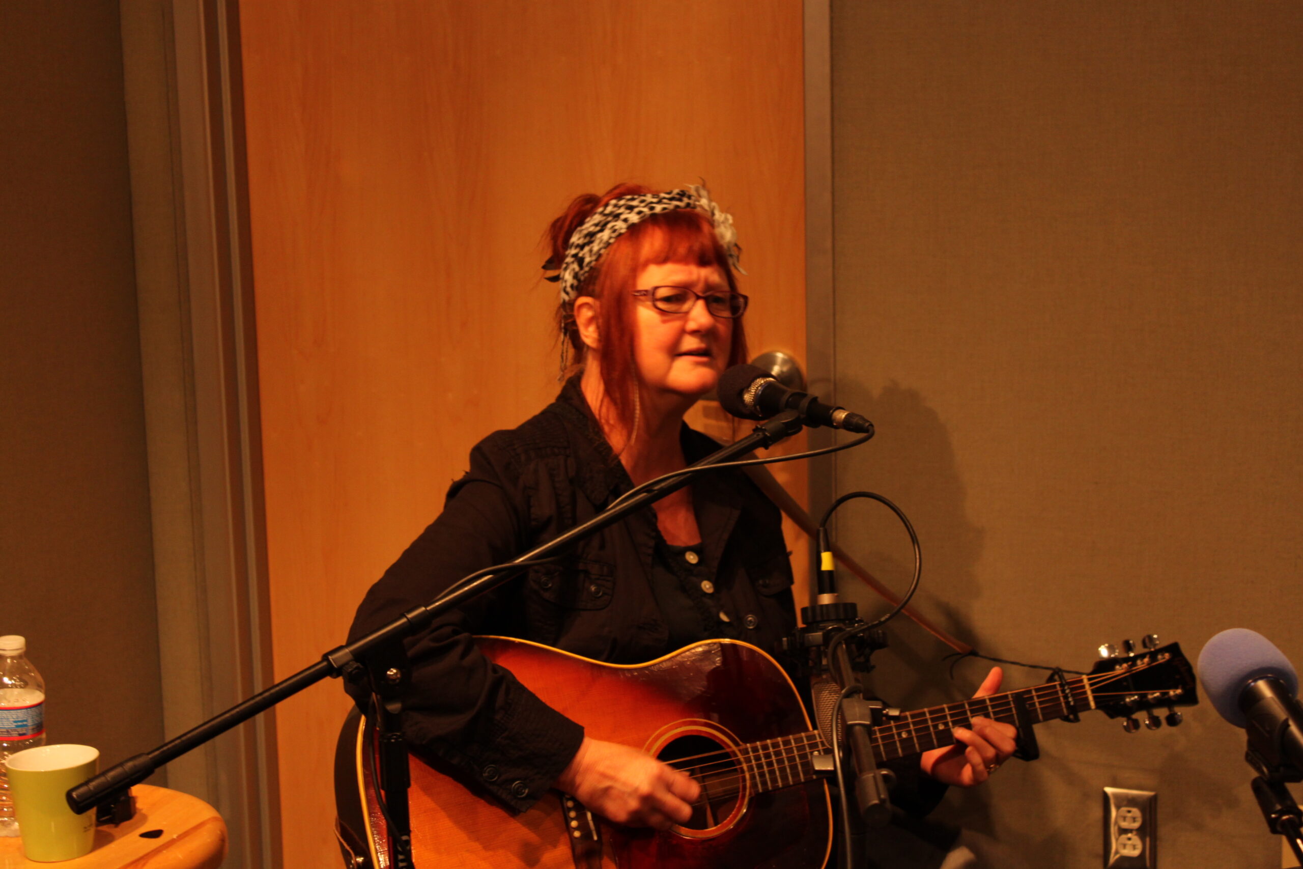 An adult playing an acoustic guitar and singing into a microphone in a radio studio