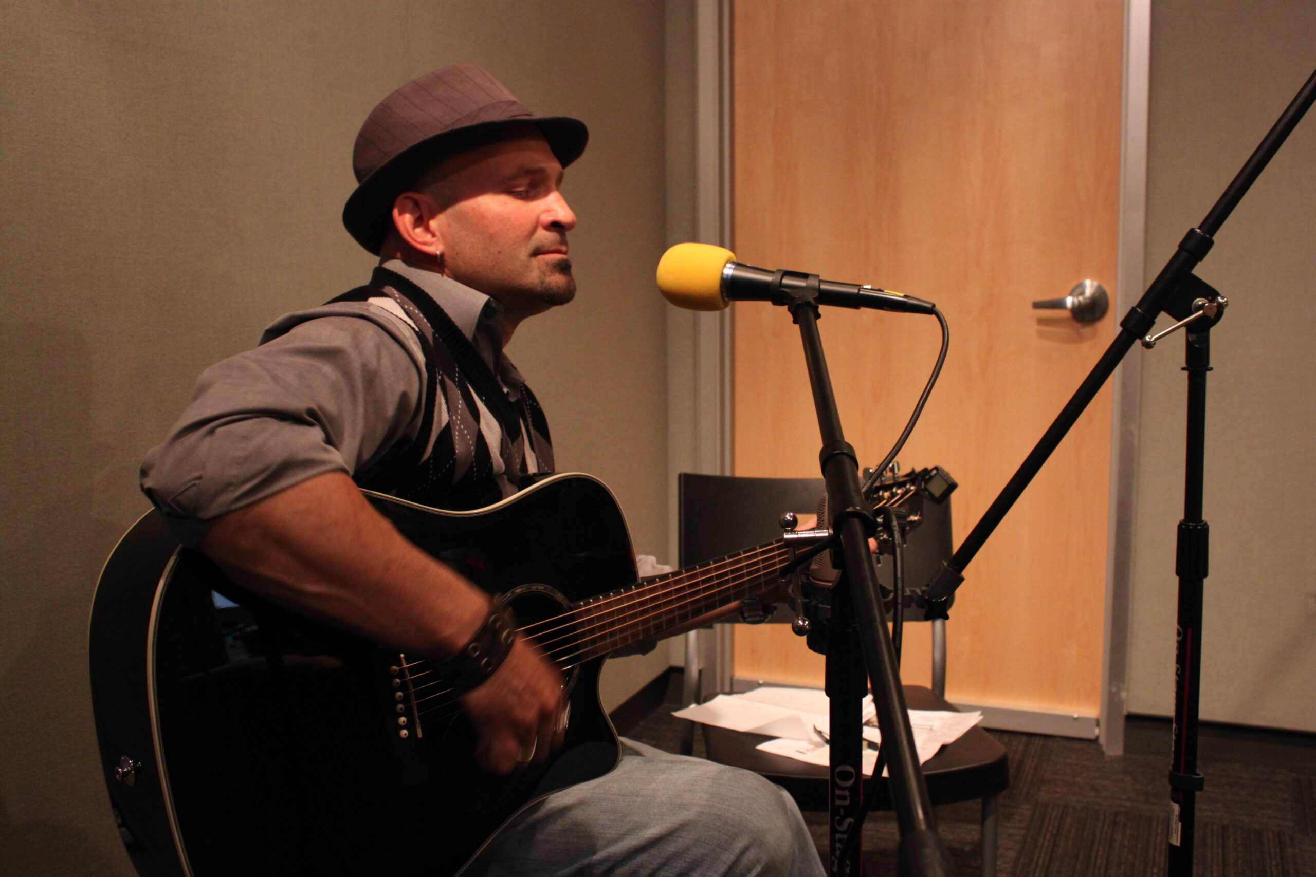 An adult playing an acoustic guitar and sitting being a microphone in a radio studio