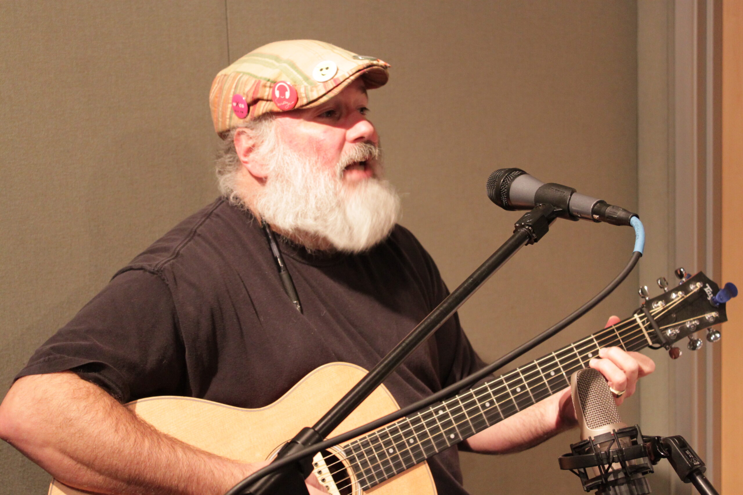 An adult playing acoustic guitar and singing into a microphone in a radio studio