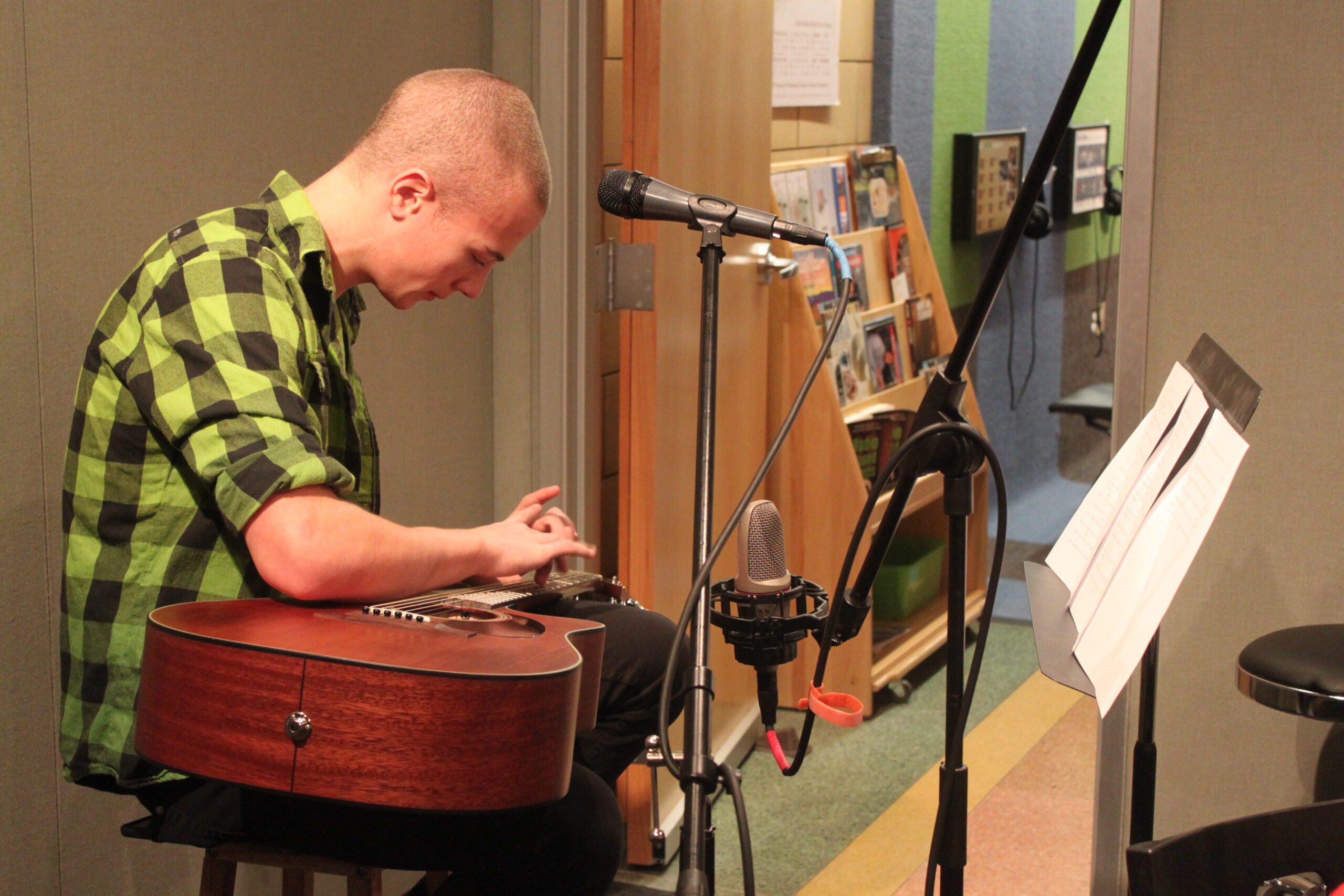 A teen sitting and looking down at an acoustic guitar in a radio studio
