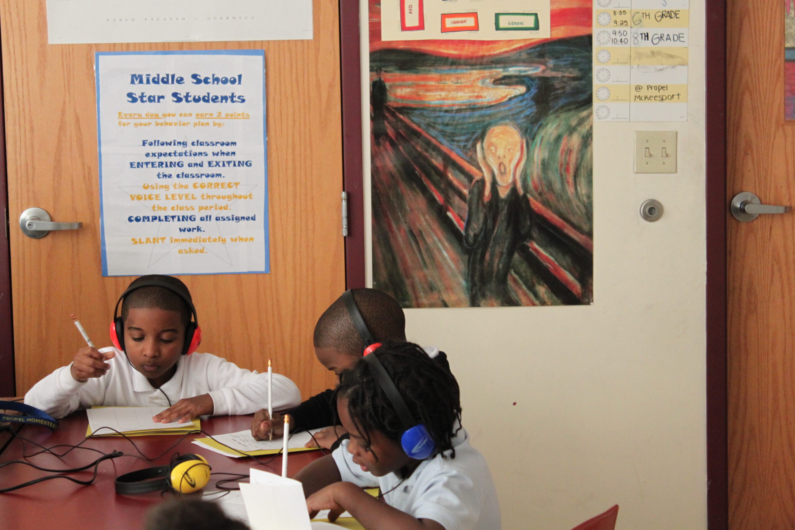 Three youth wearing headphones writing on pieces of paper in a classroom