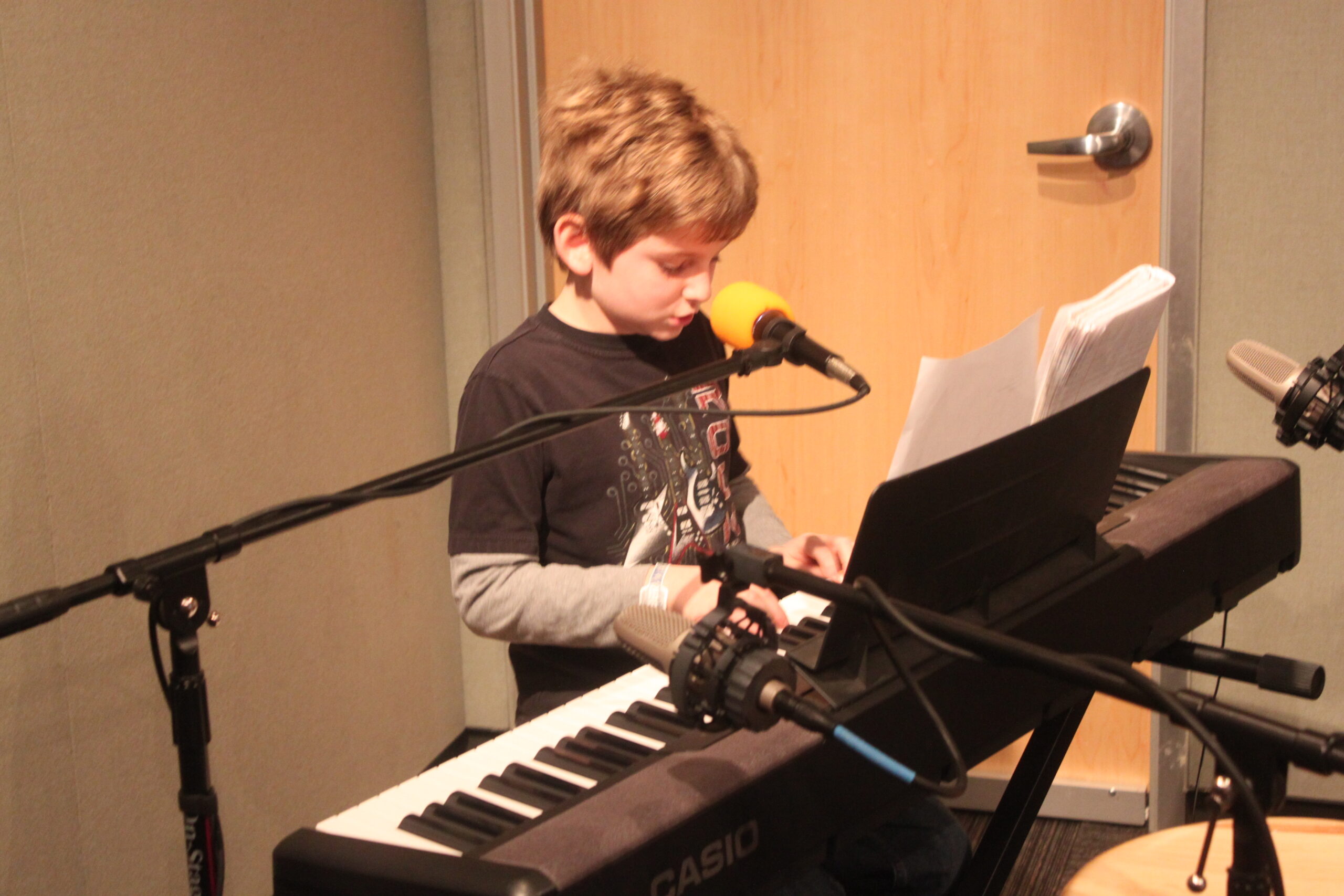 A youth playing a piano keyboard and standing behind a microphone in a radio studio