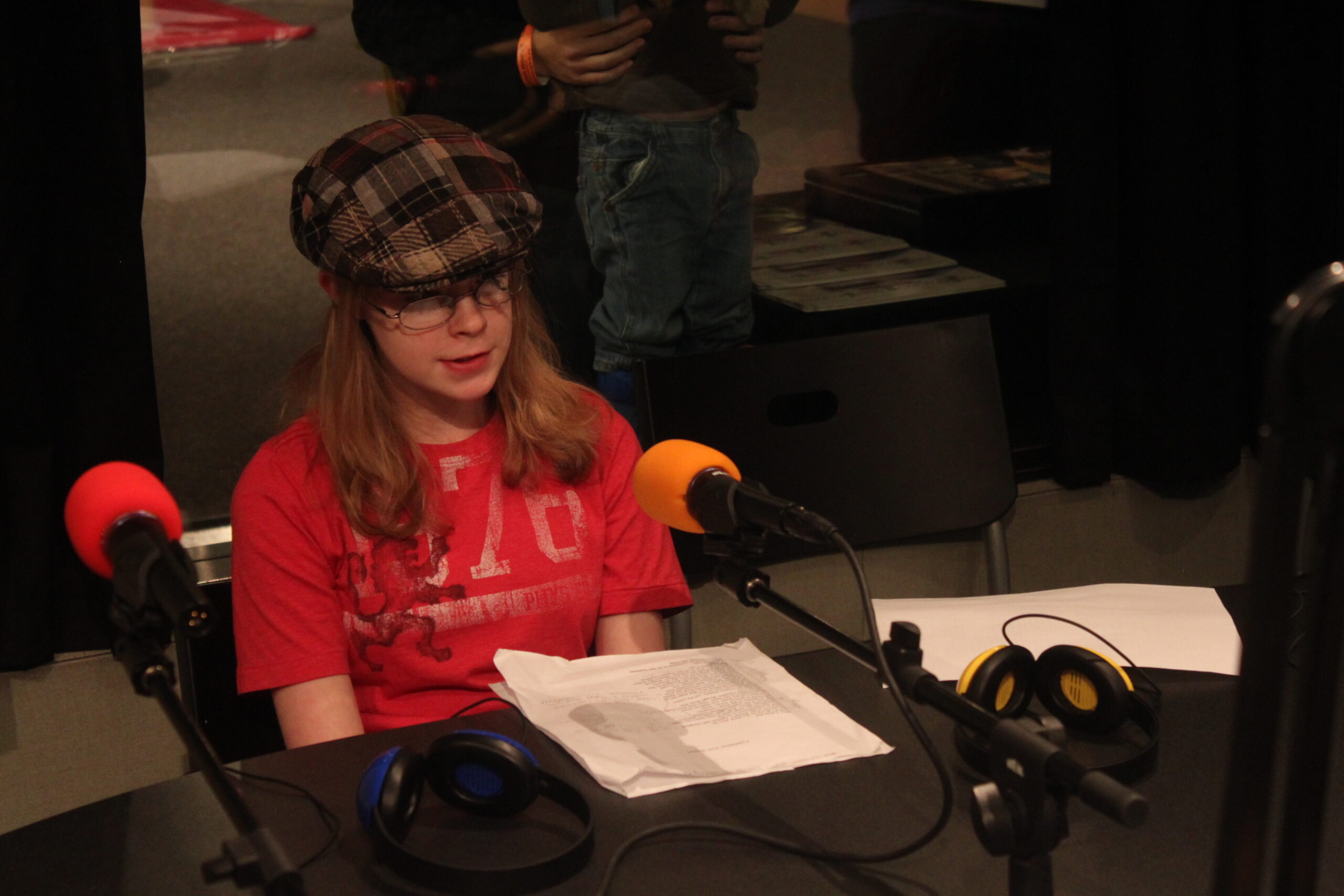 A teen sitting behind a piece of paper and a microphone in a radio studio
