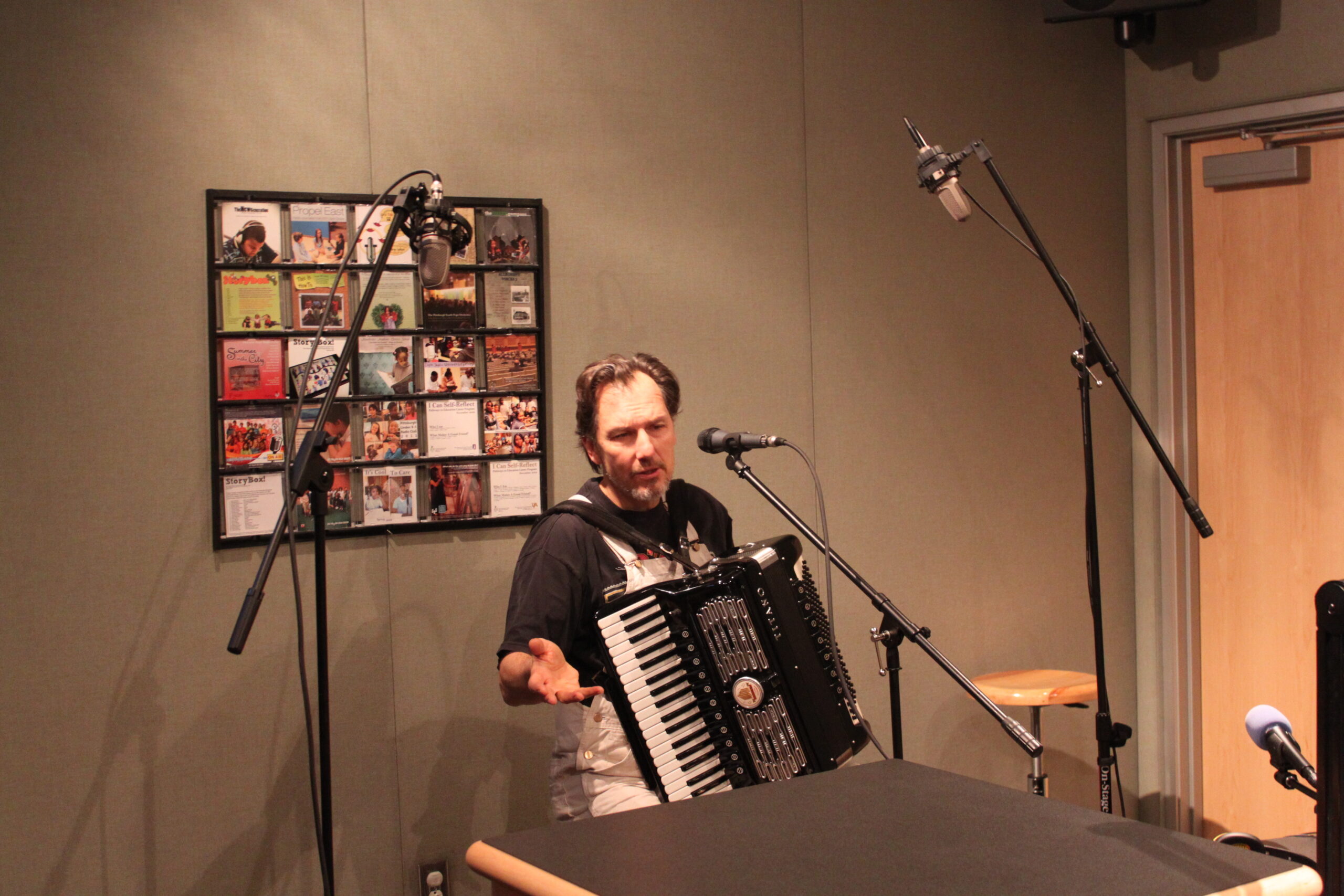 An adult playing an accordion while sitting behind microphones in a radio studio
