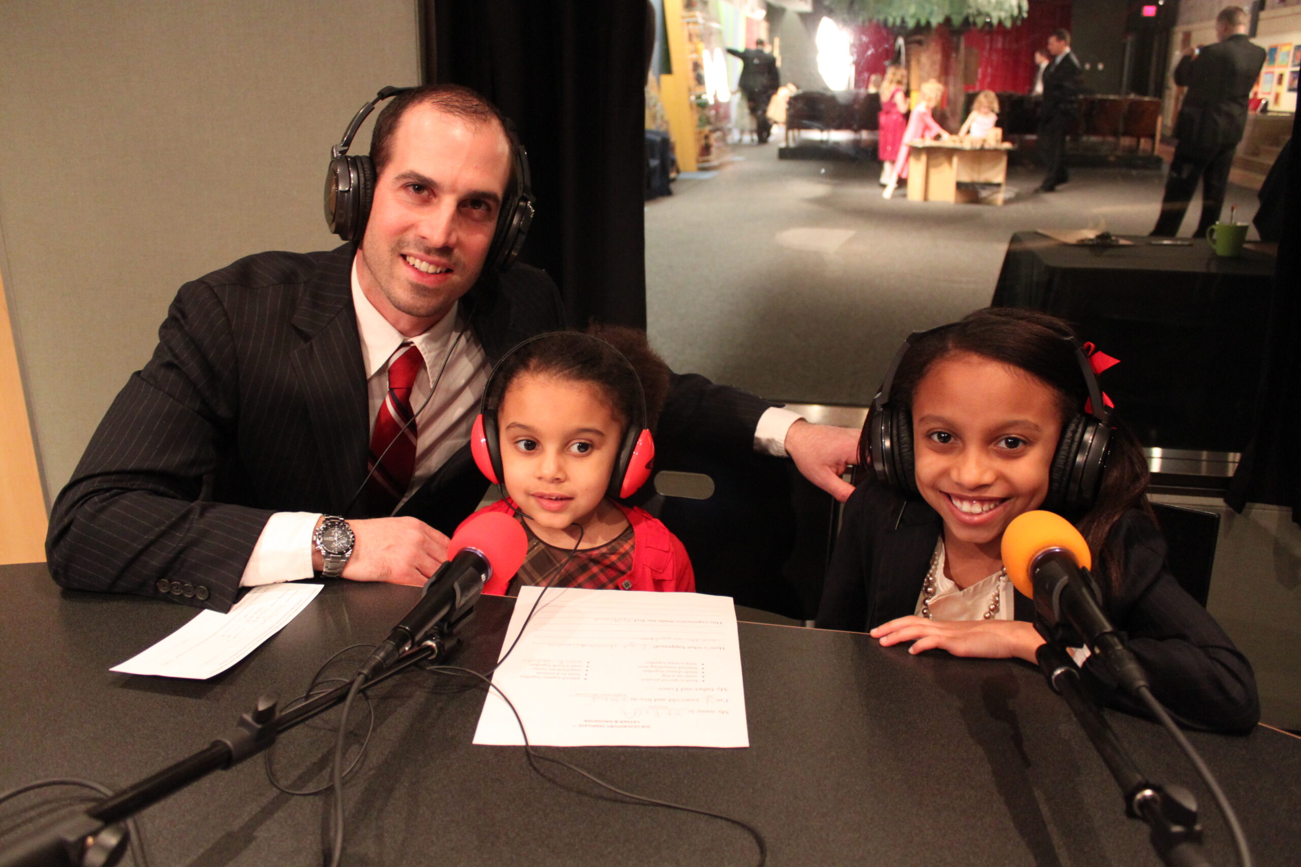 Two youth and an adult wearing headphones sitting behind microphones in a radio studio