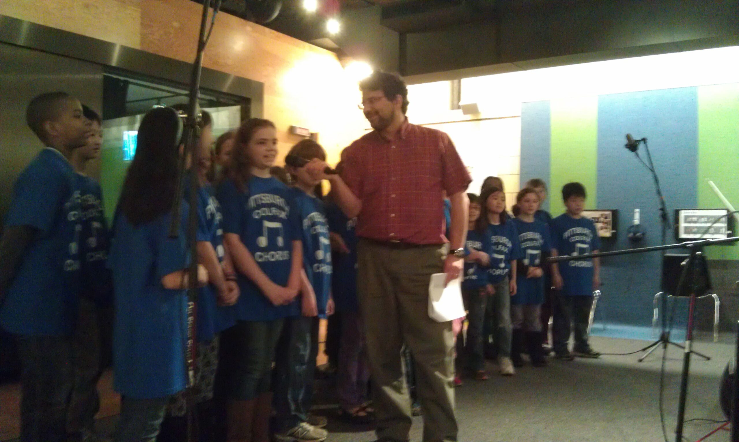 An adult interviewing a choir of youth in front of a radio studio