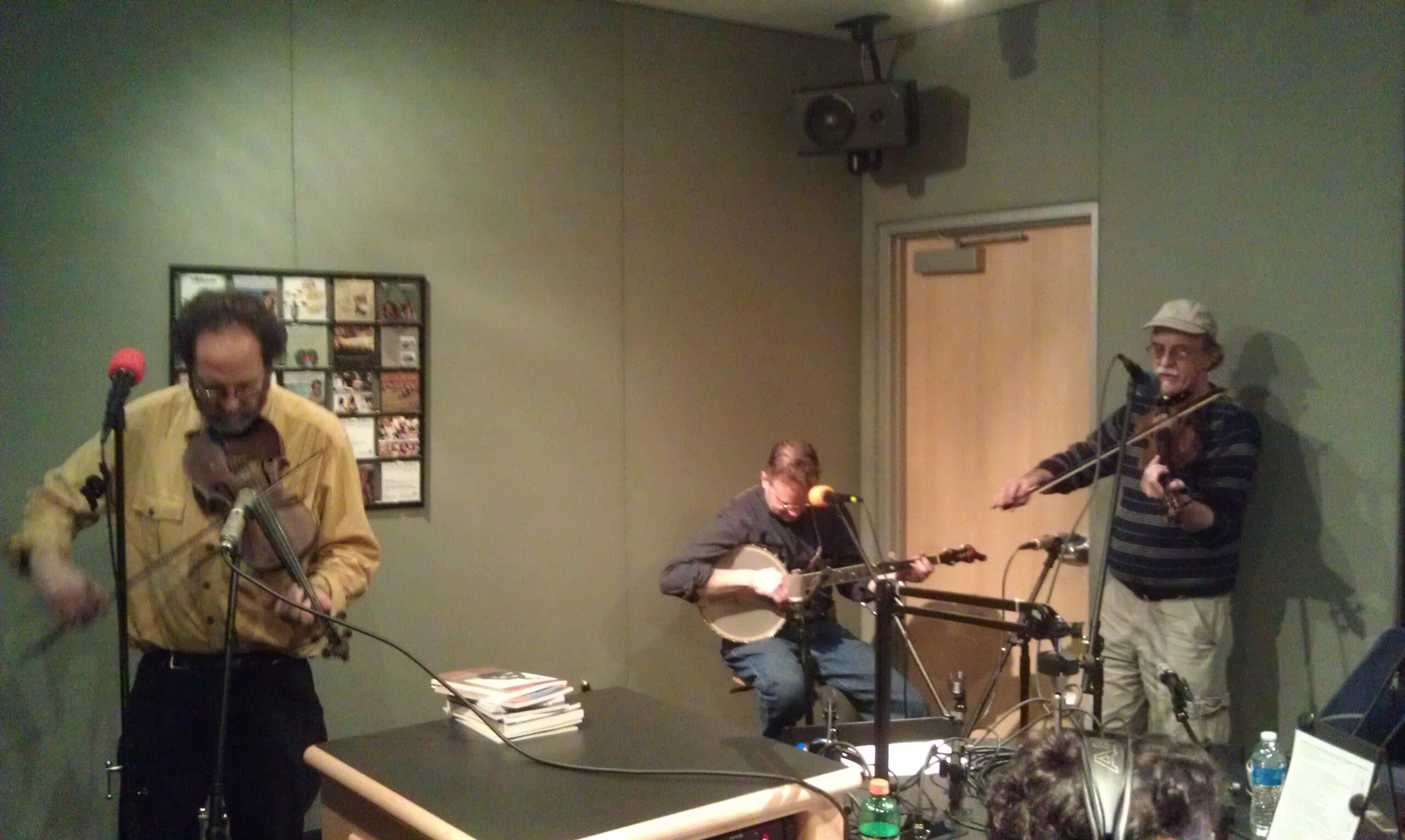 Two adults playing violins and an adult playing banjo in a radio studio