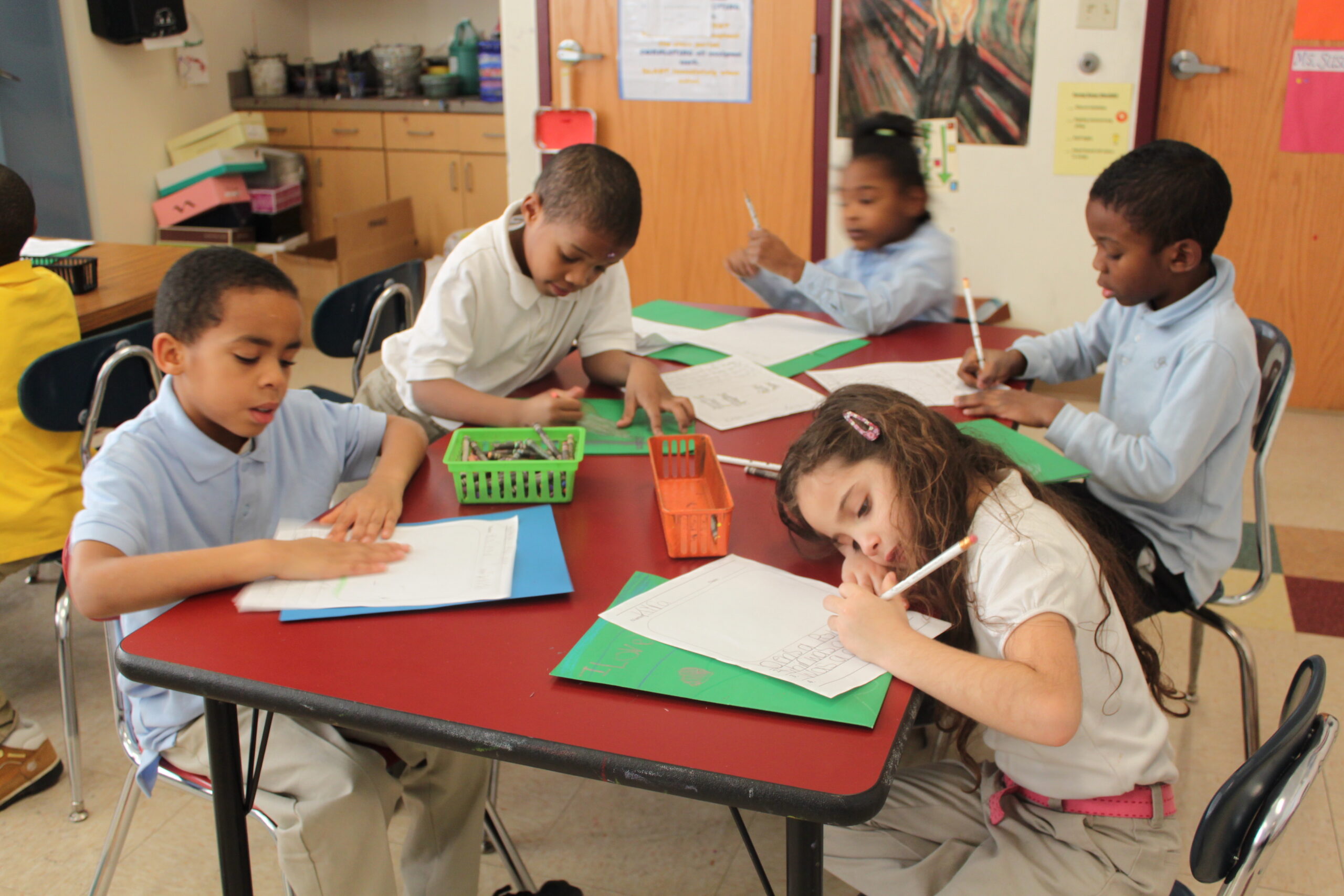 Five youth writing on pieces of paper on a classroom table