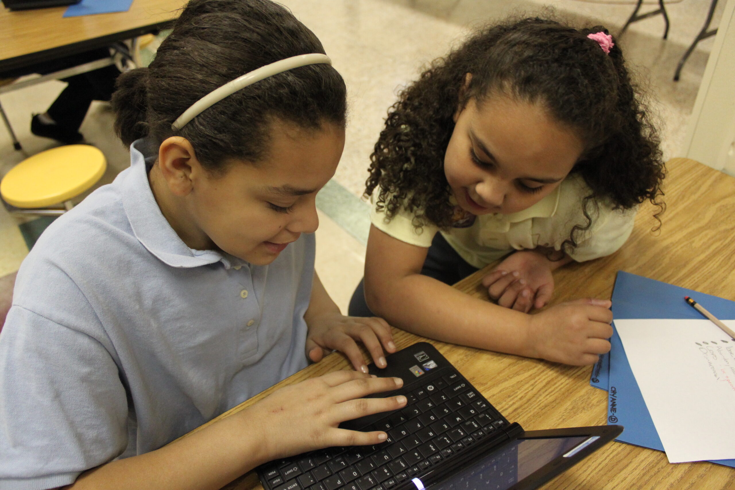 Two youth looking at a laptop computer on a classroom desk