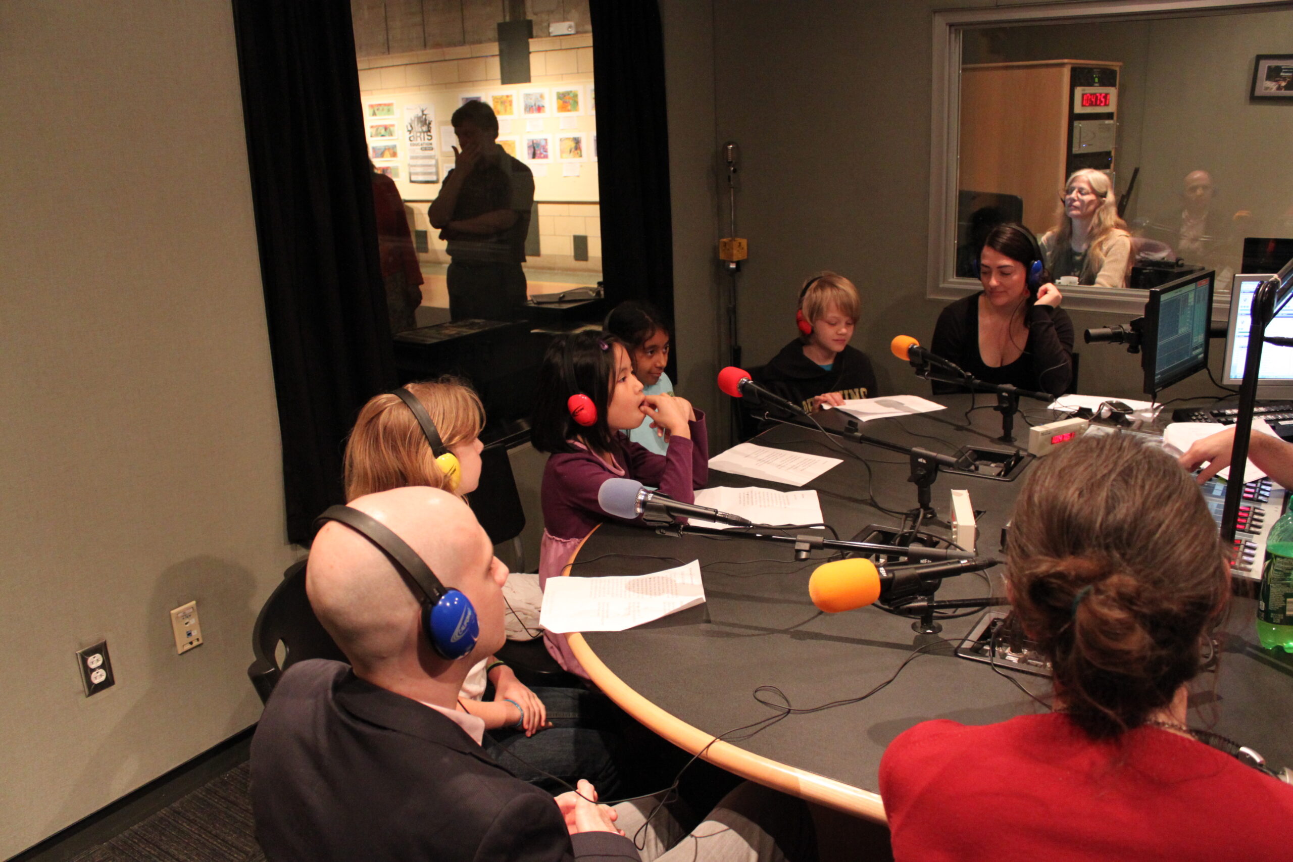 Four youth and three adults wearing headphones speaking into microphones in a radio studio