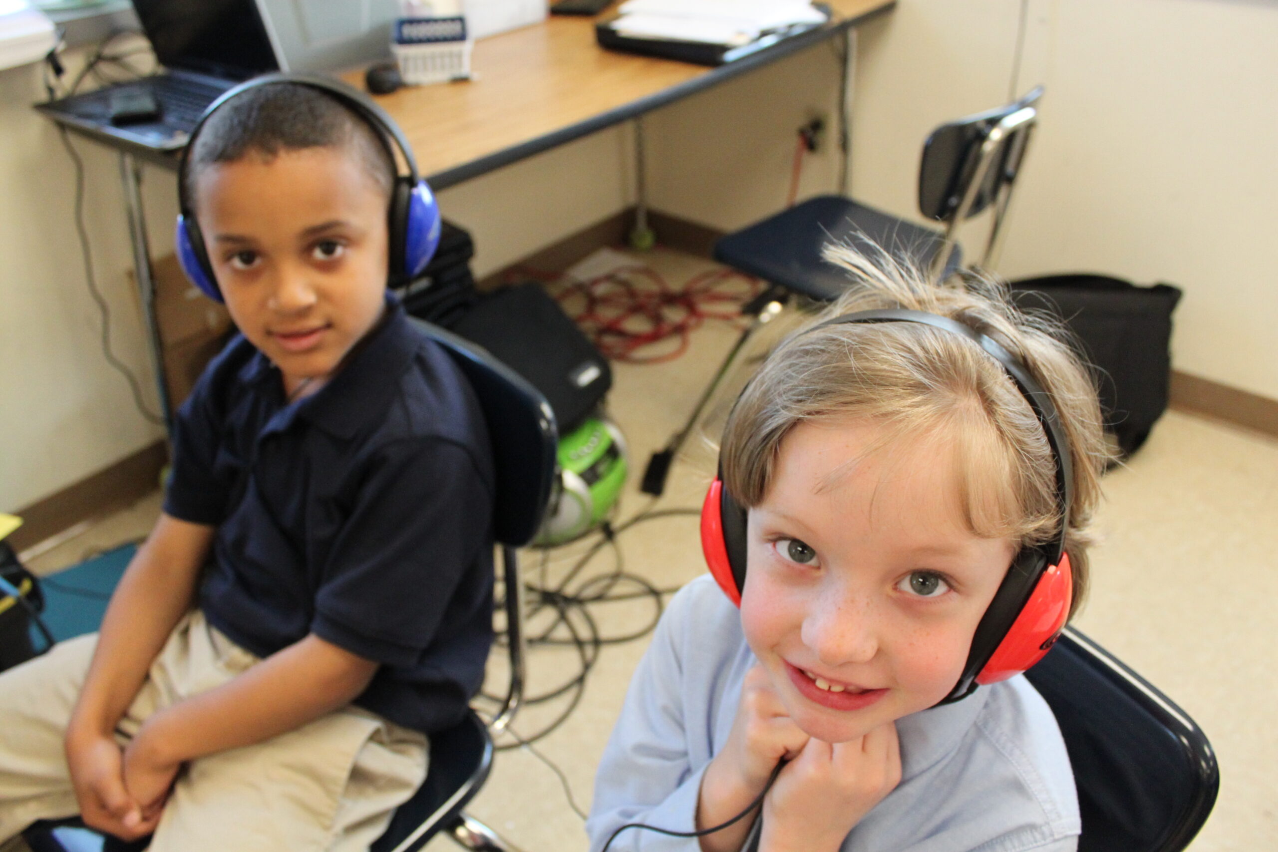 Two youth wearing headphones looking up at the camera in a classroom