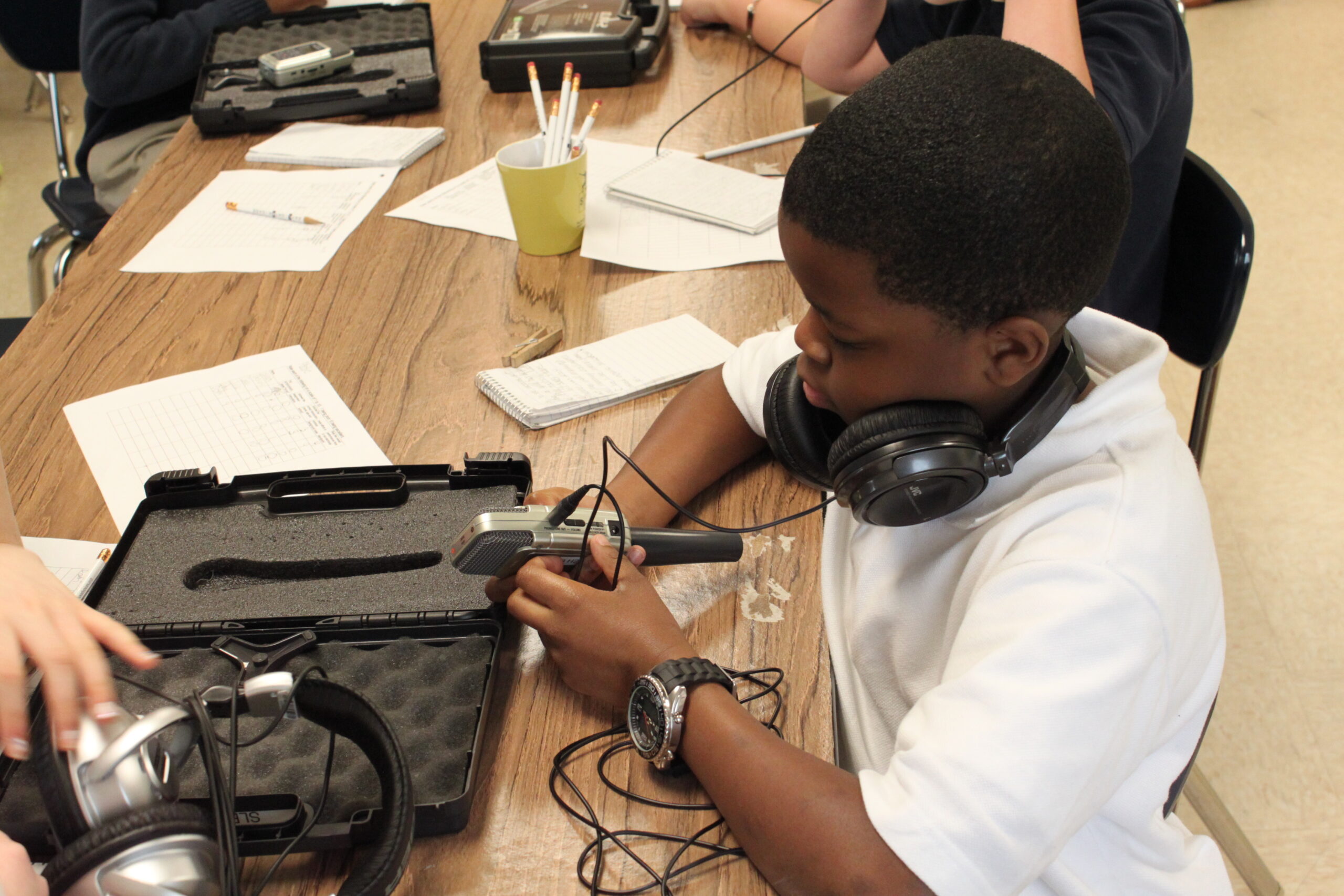 A youth wearing headphones holding a portable recorder while sitting at a table