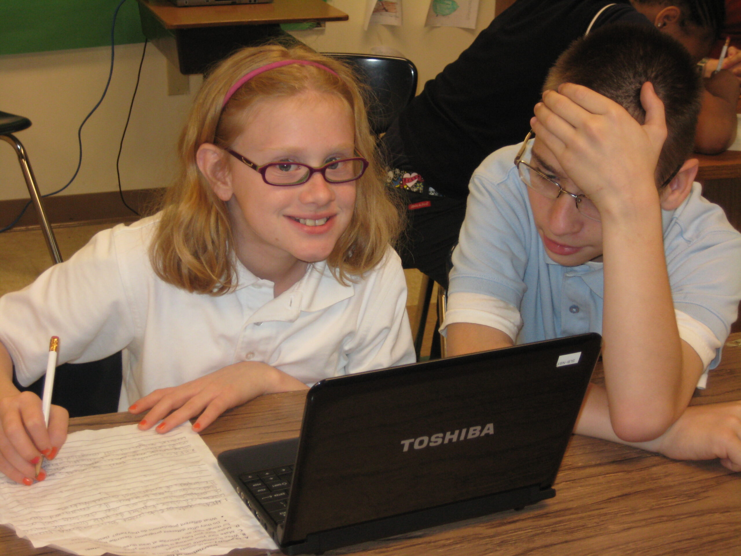 Two youth looking at a laptop computer on a classroom table