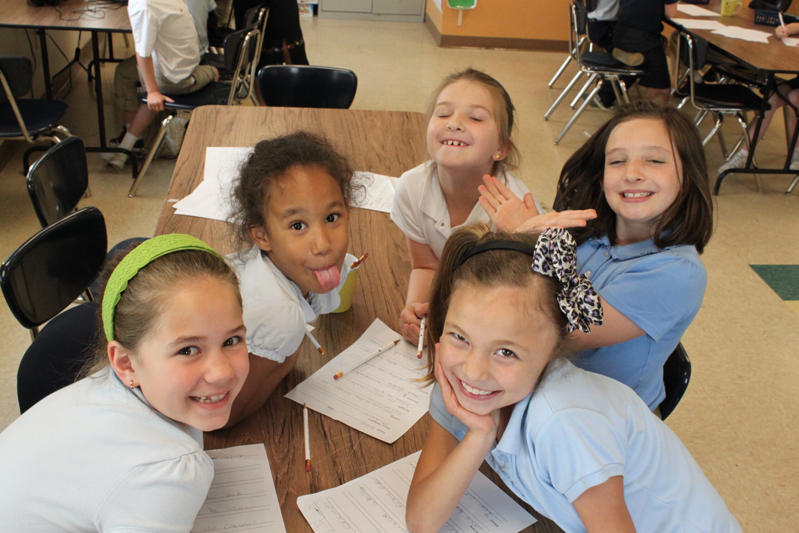 Five youth smiling at the camera and sitting around pieces of paper on a classroom table