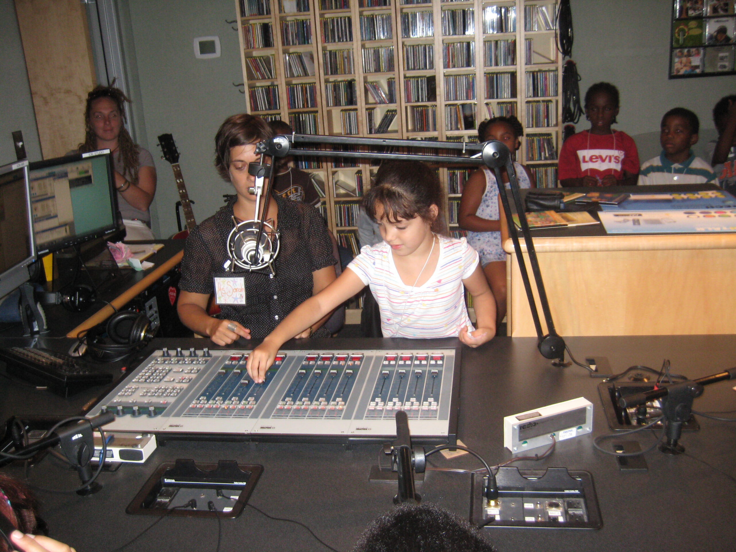 Two youth sitting behind an audio mixer in a radio studio