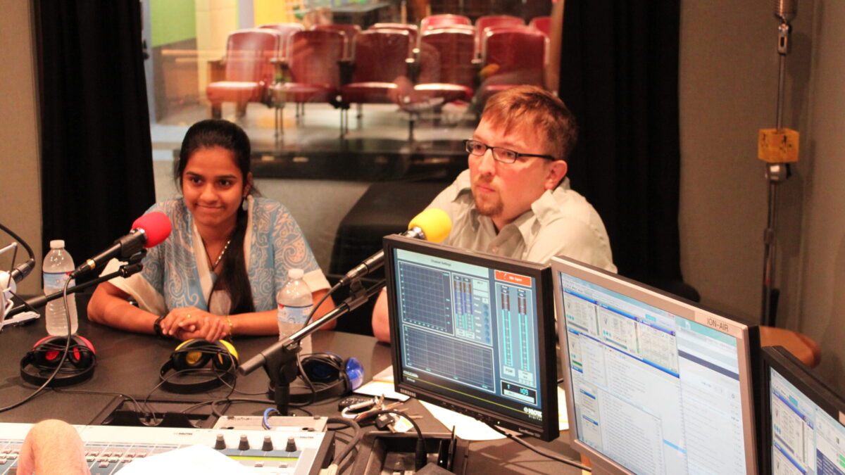 Two adults speaking into microphones in a radio studio