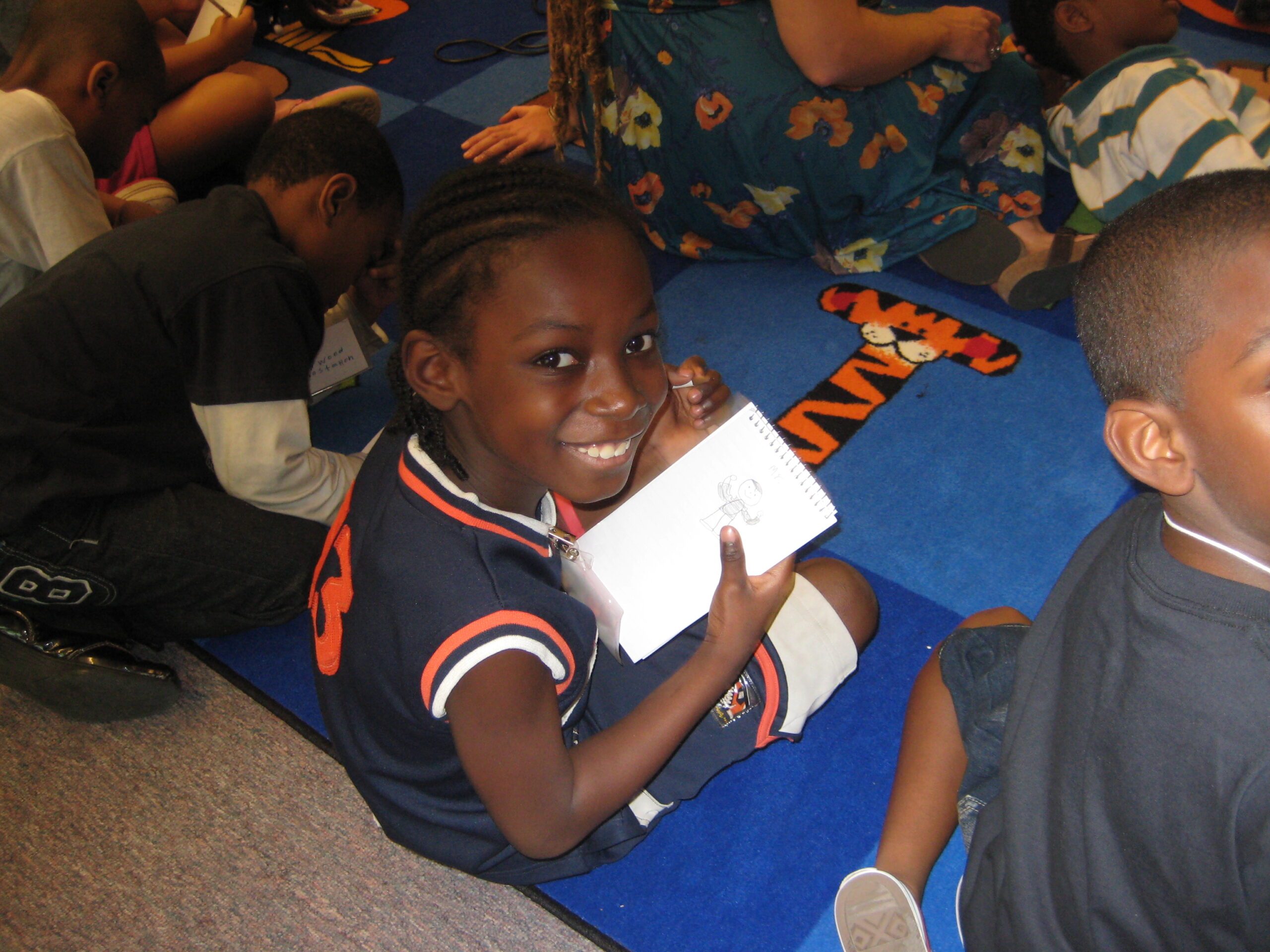 A youth smiling at the camera while holding a piece of paper while sitting at a blue table