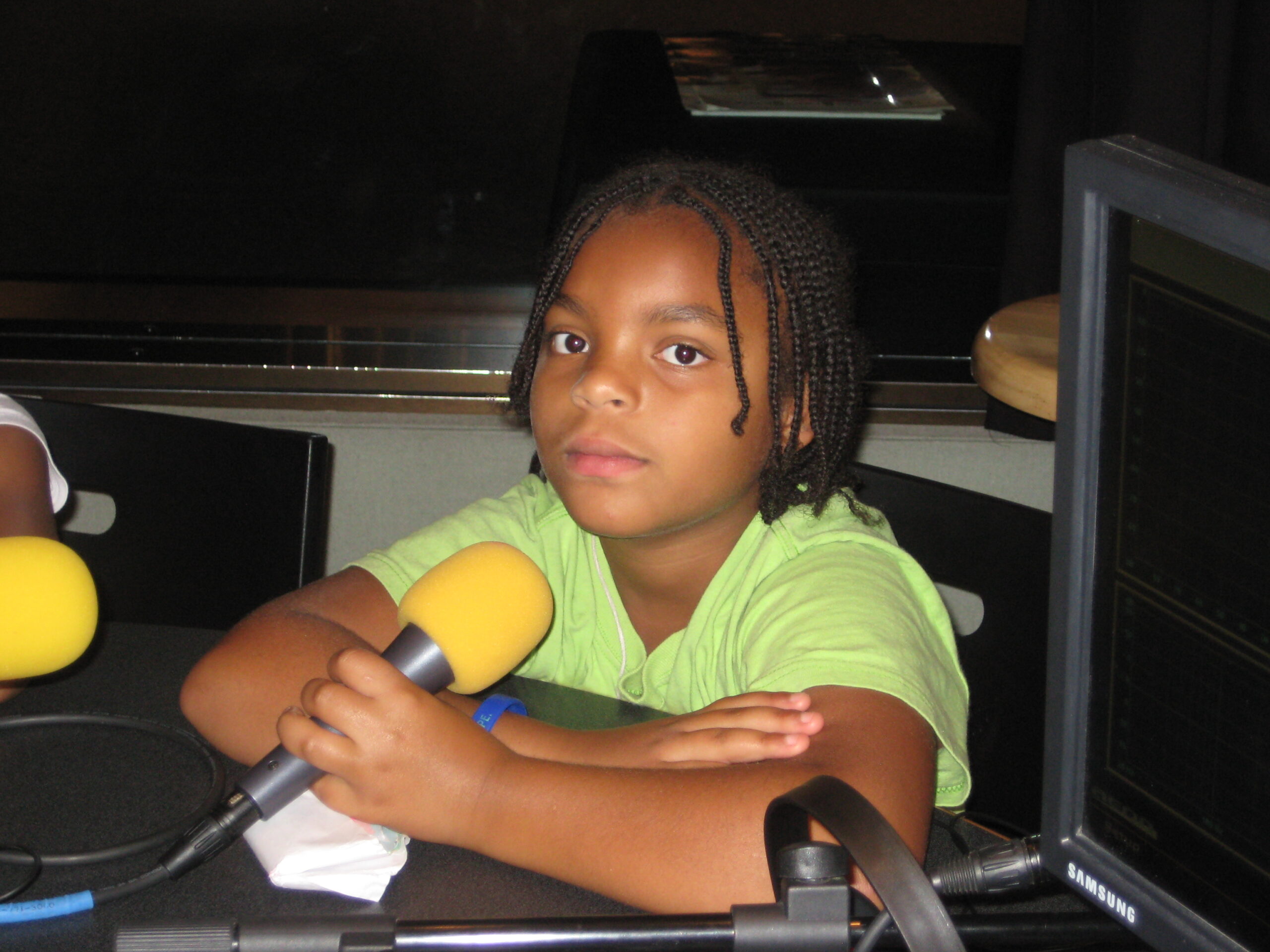 A youth sitting behind a yellow microphone in a radio studio