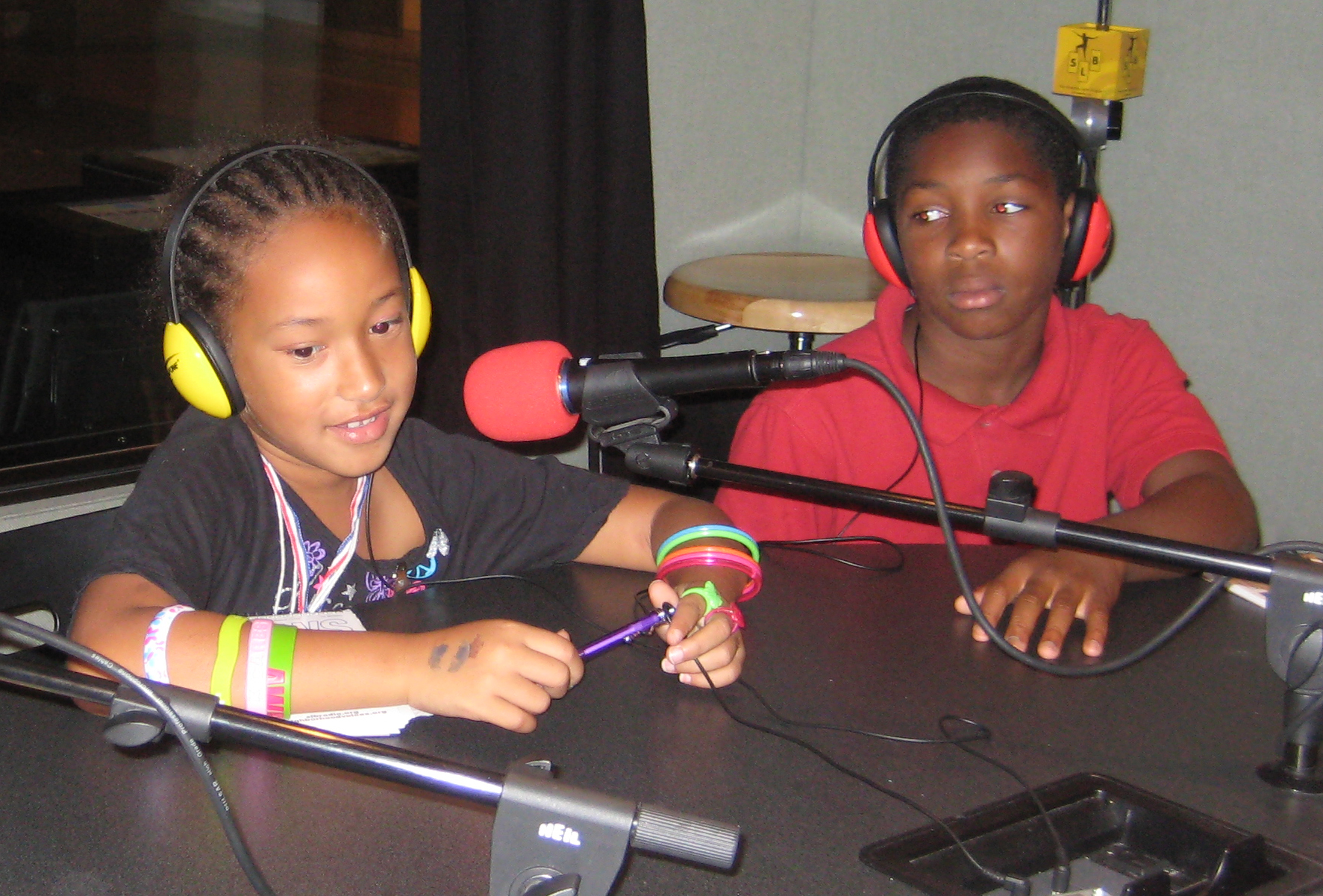 Two youth wearing headphones speaking into microphones in a radio studio