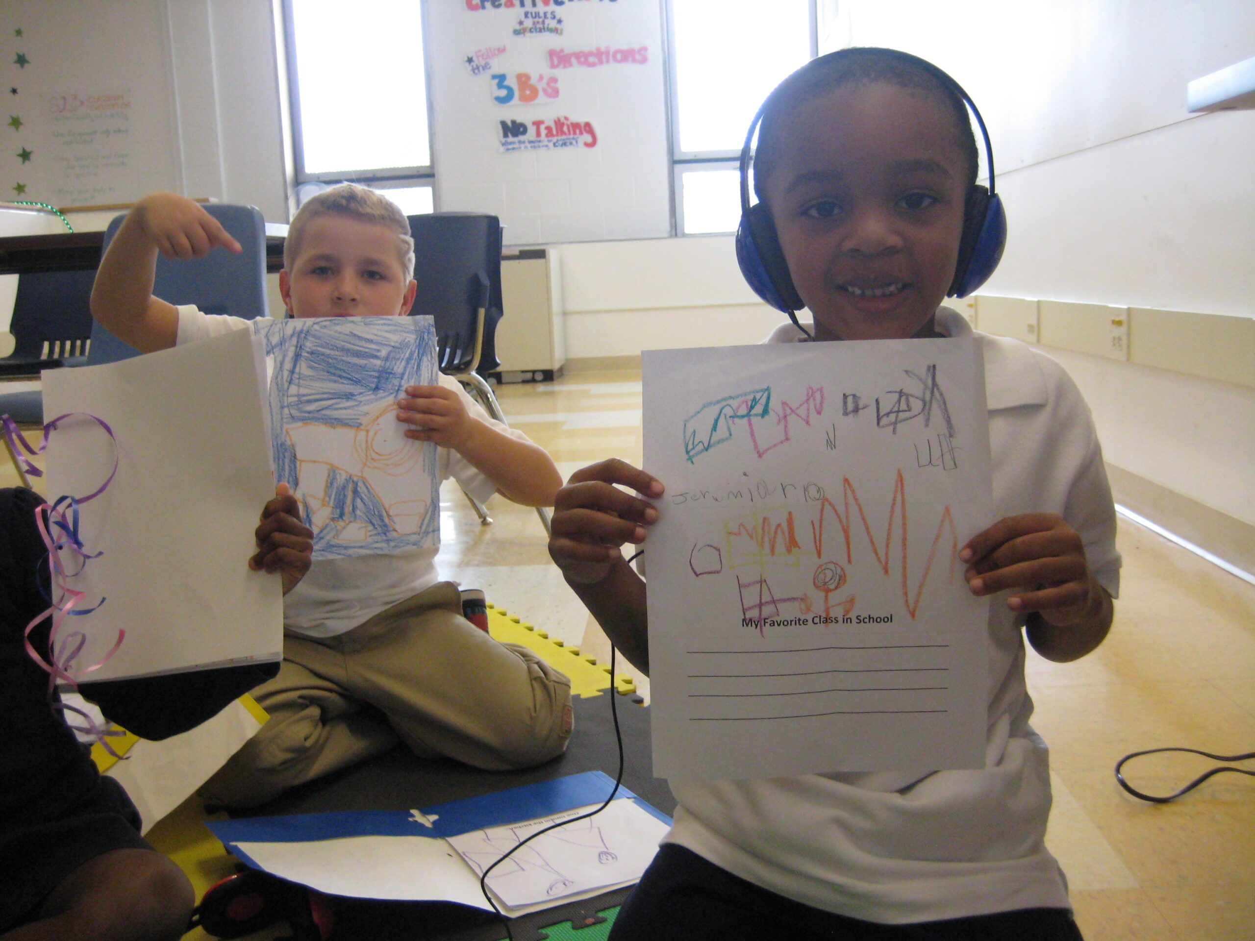 Three youth holding up pieces of paper to the camera in a classroom, one of the youth wearing headphones