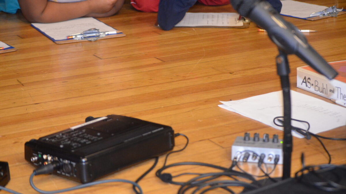 Recording equipment surrounded by pieces of paper and a microphone on a wooden floor