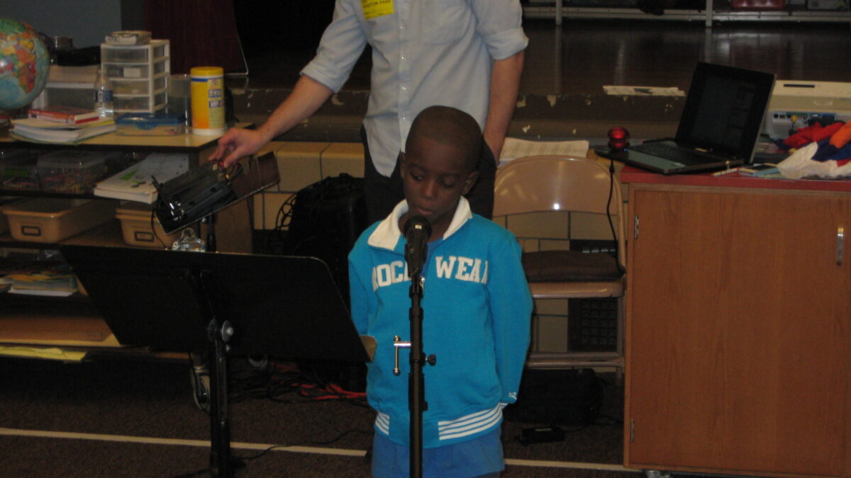 Spring Hill K-5 2013 An adult standing behind a youth speaking into a microphone while looking at a music stand