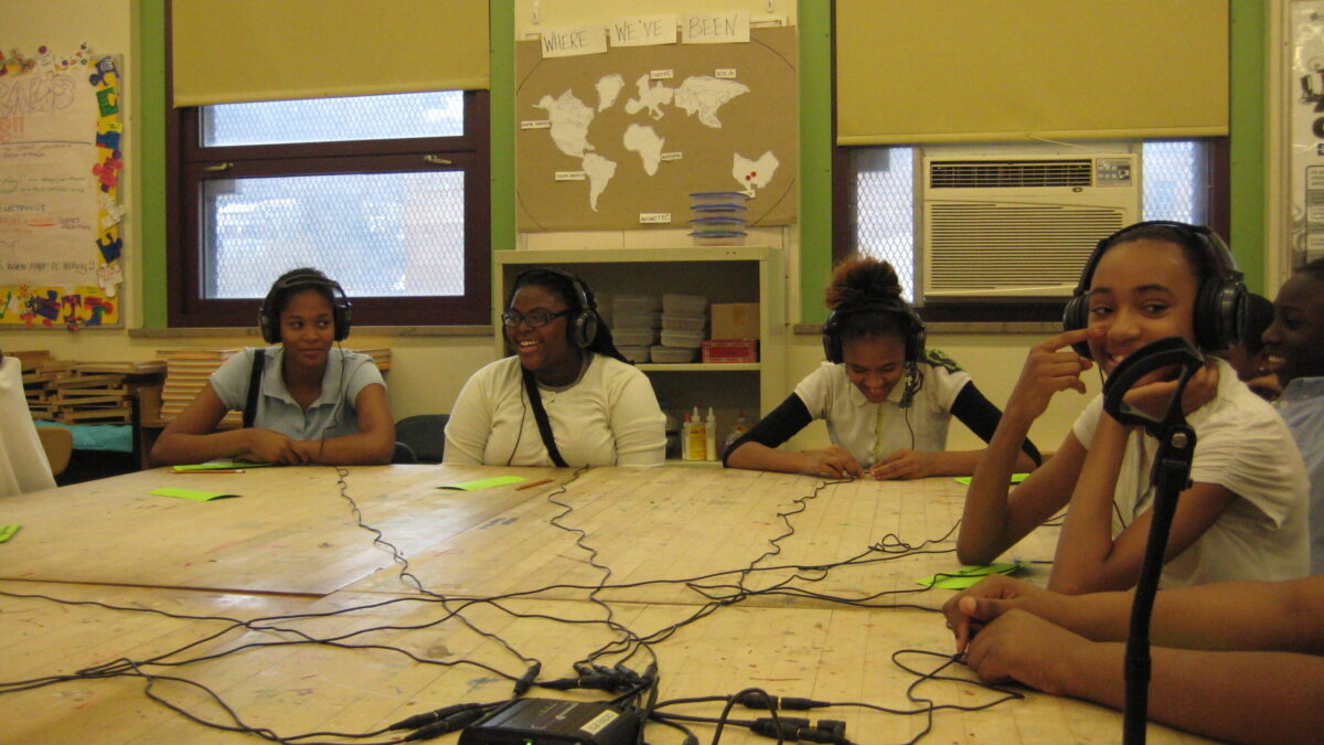 Four youth wearing headphones connected to a headphone splitter on a table in a classroom