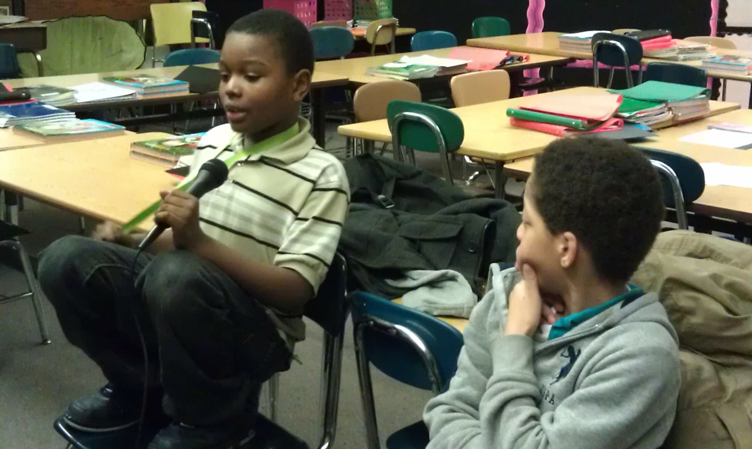 A youth looking at another youth speaking into a microphone in a classroom