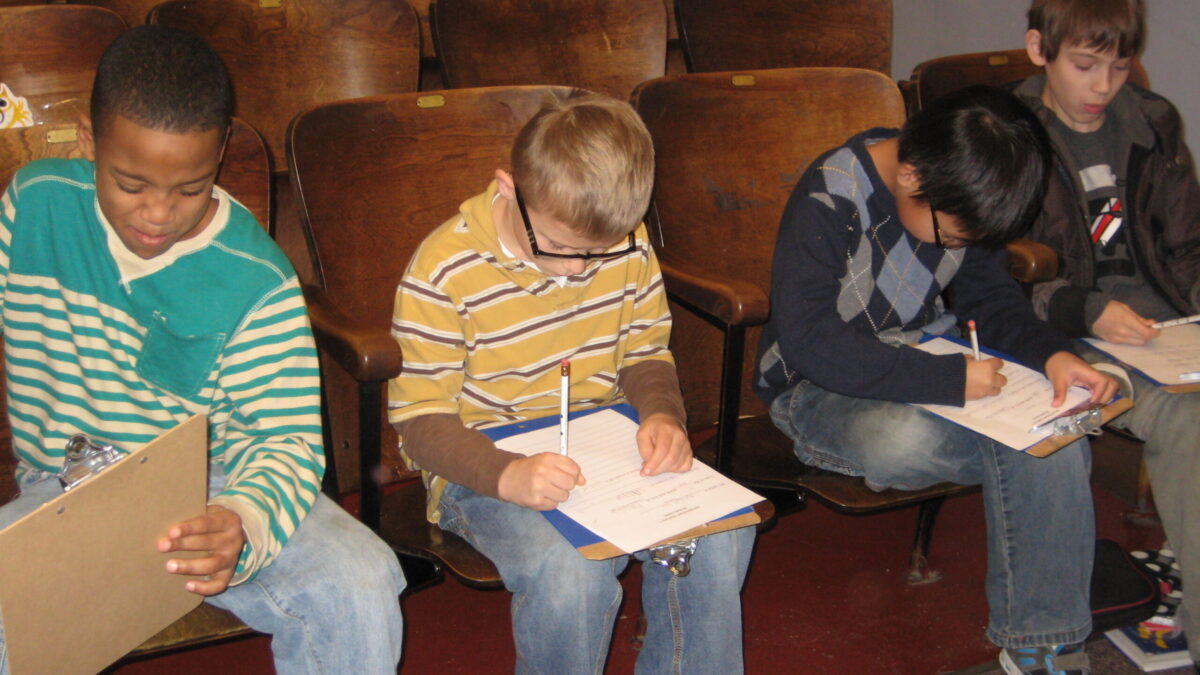 Four youth writing on clipboards while sitting in auditorium seats