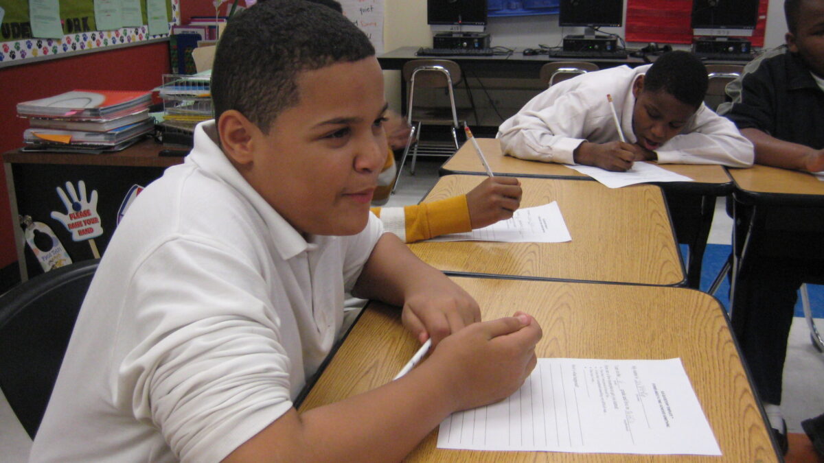 Two youth writing on pieces of paper in a classroom