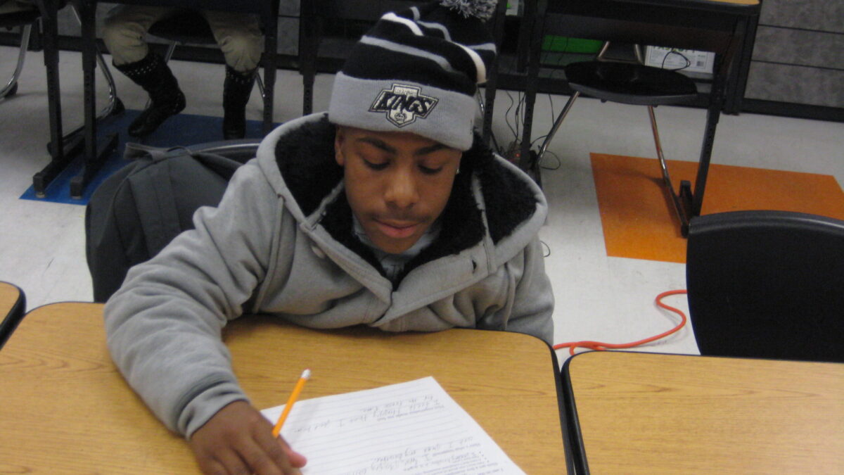 A youth writing on a piece of paper on a classroom desk